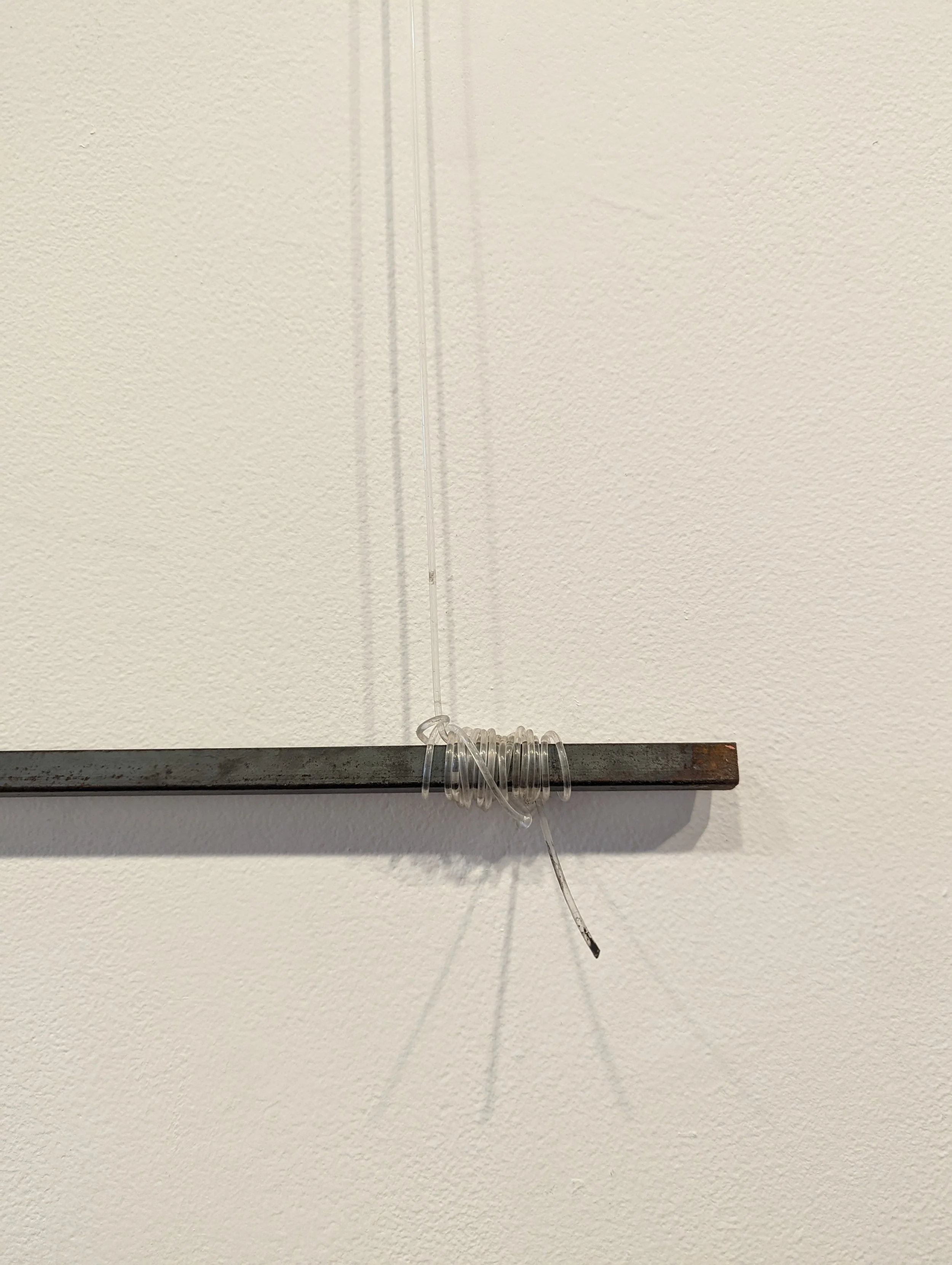 A clear plastic tube with a coiled section at the bottom, hanging vertically on a wall.