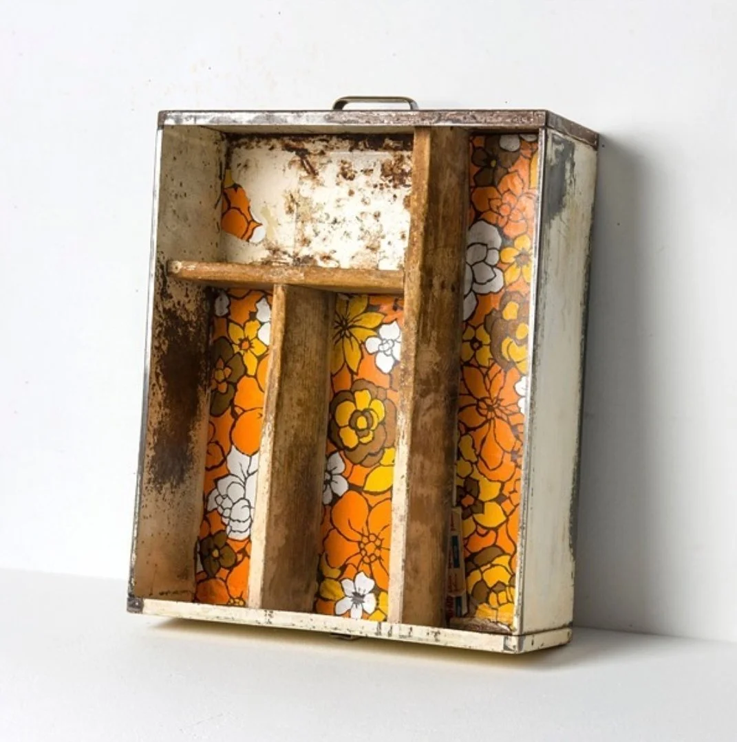 A vintage metal cigarette and jewelry box with orange, yellow, white, and brown floral wallpaper inside, showing signs of rust and age.