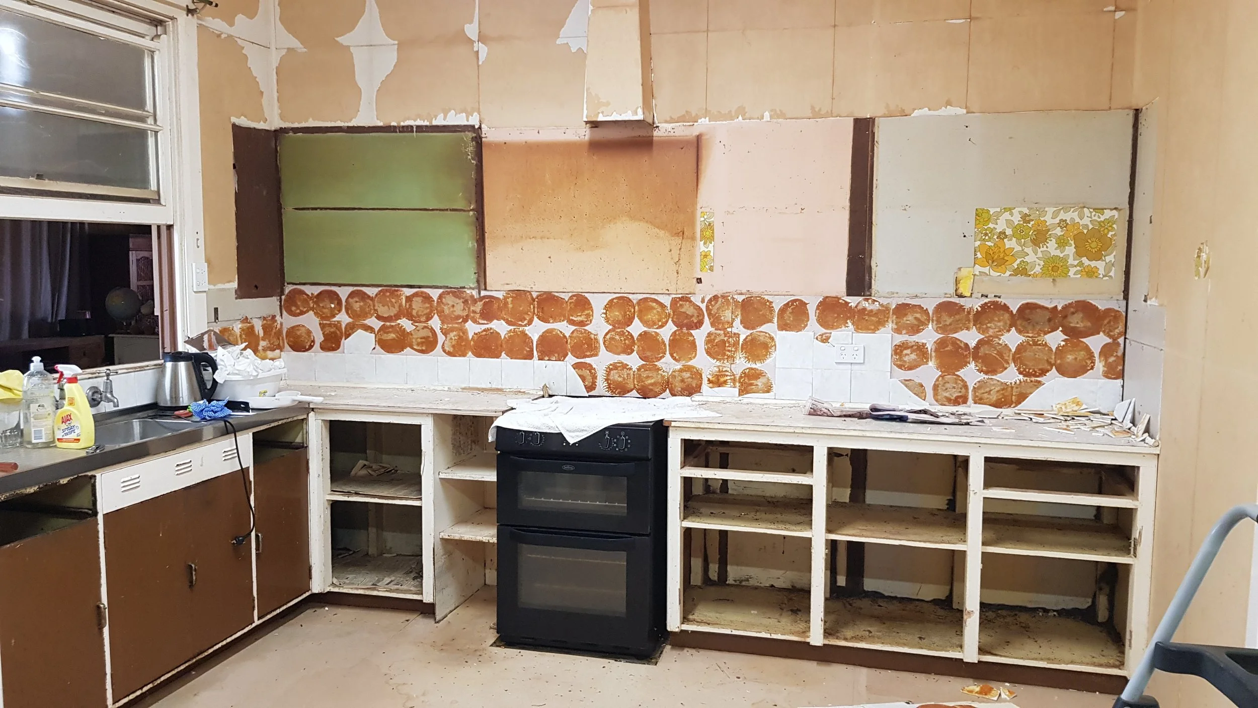 Kitchen with unfinished cabinetry and backsplash removal, showing exposed wall and peeling paint.