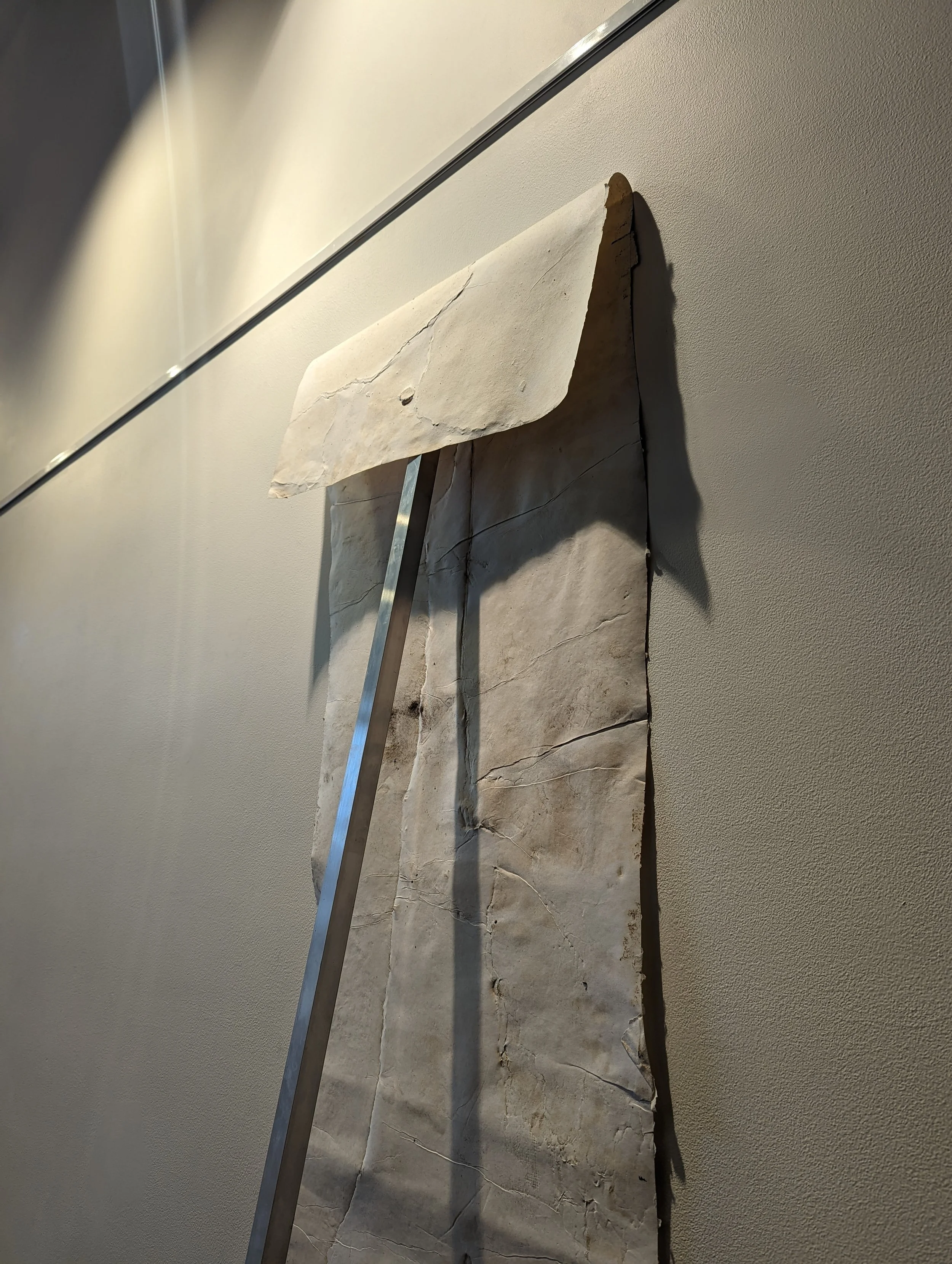 A large piece of cracked, broken marble or stone with a metal rod leaning against it, mounted on a beige wall.