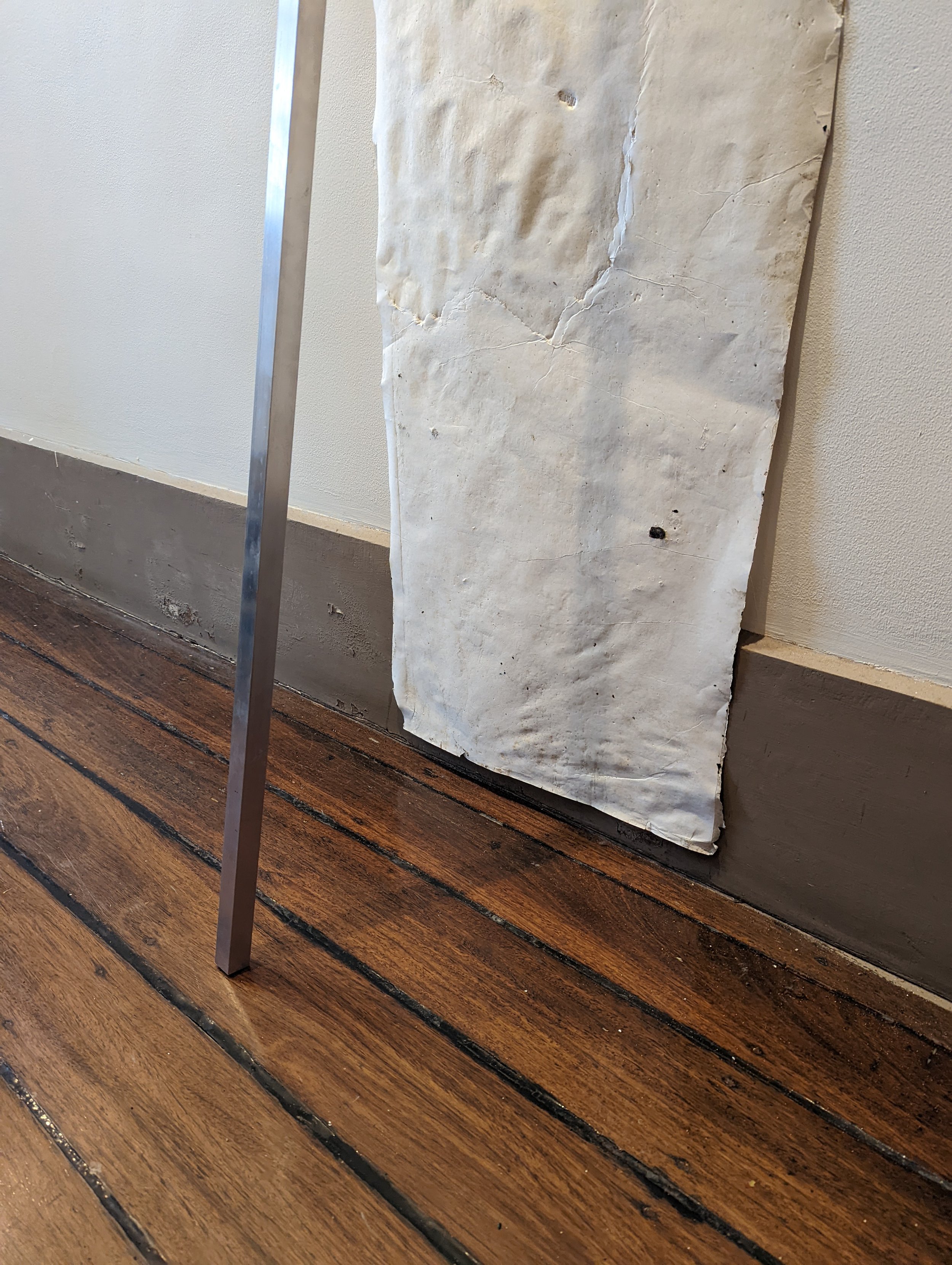 A piece of white marble with natural veining, mounted vertically on a wall with a metal stand, placed on a wooden floor in a room.
