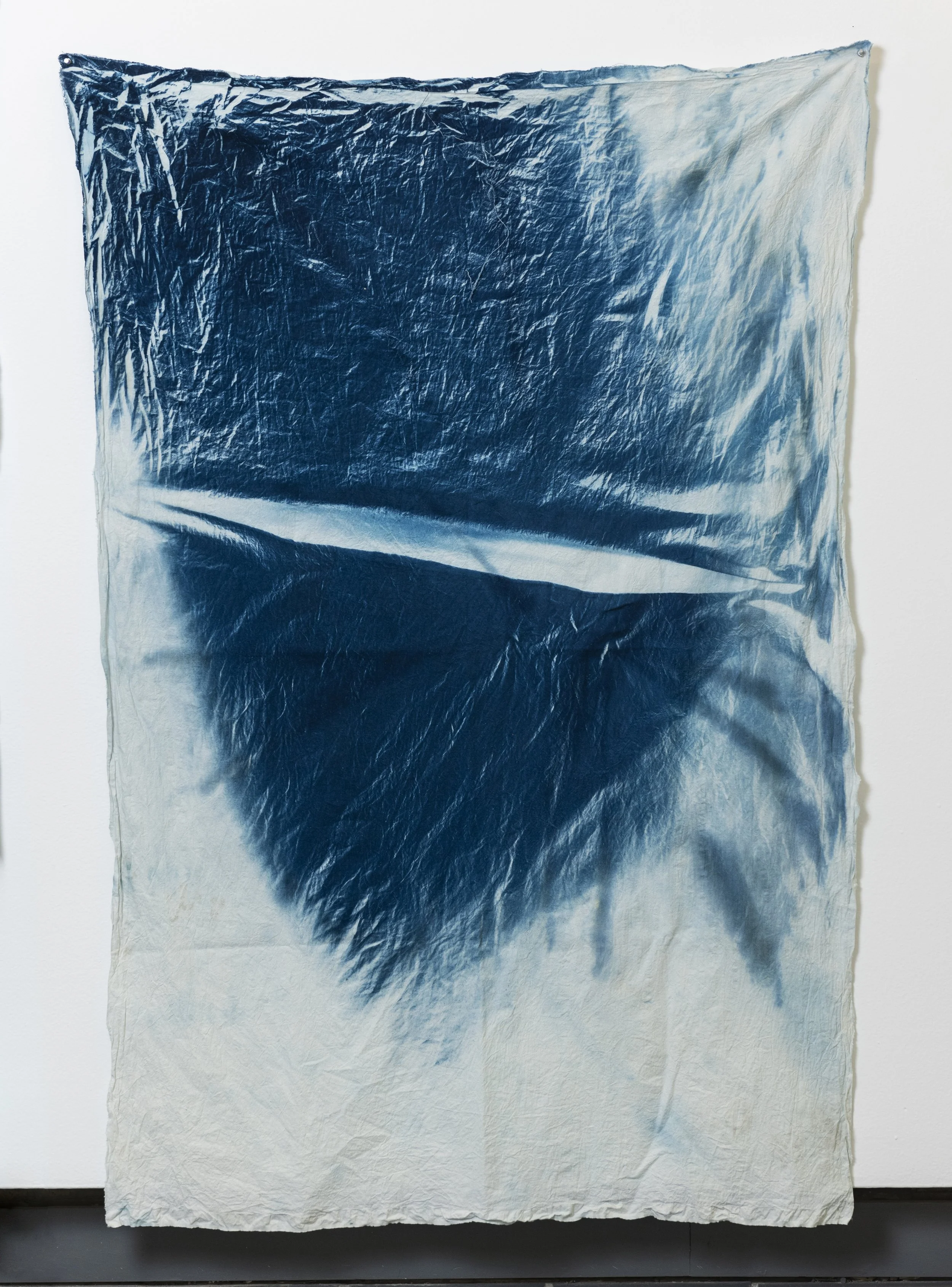 A large piece of fabric with an ombre gradient from dark blue at the top to light cream at the bottom, hanging against a white wall.