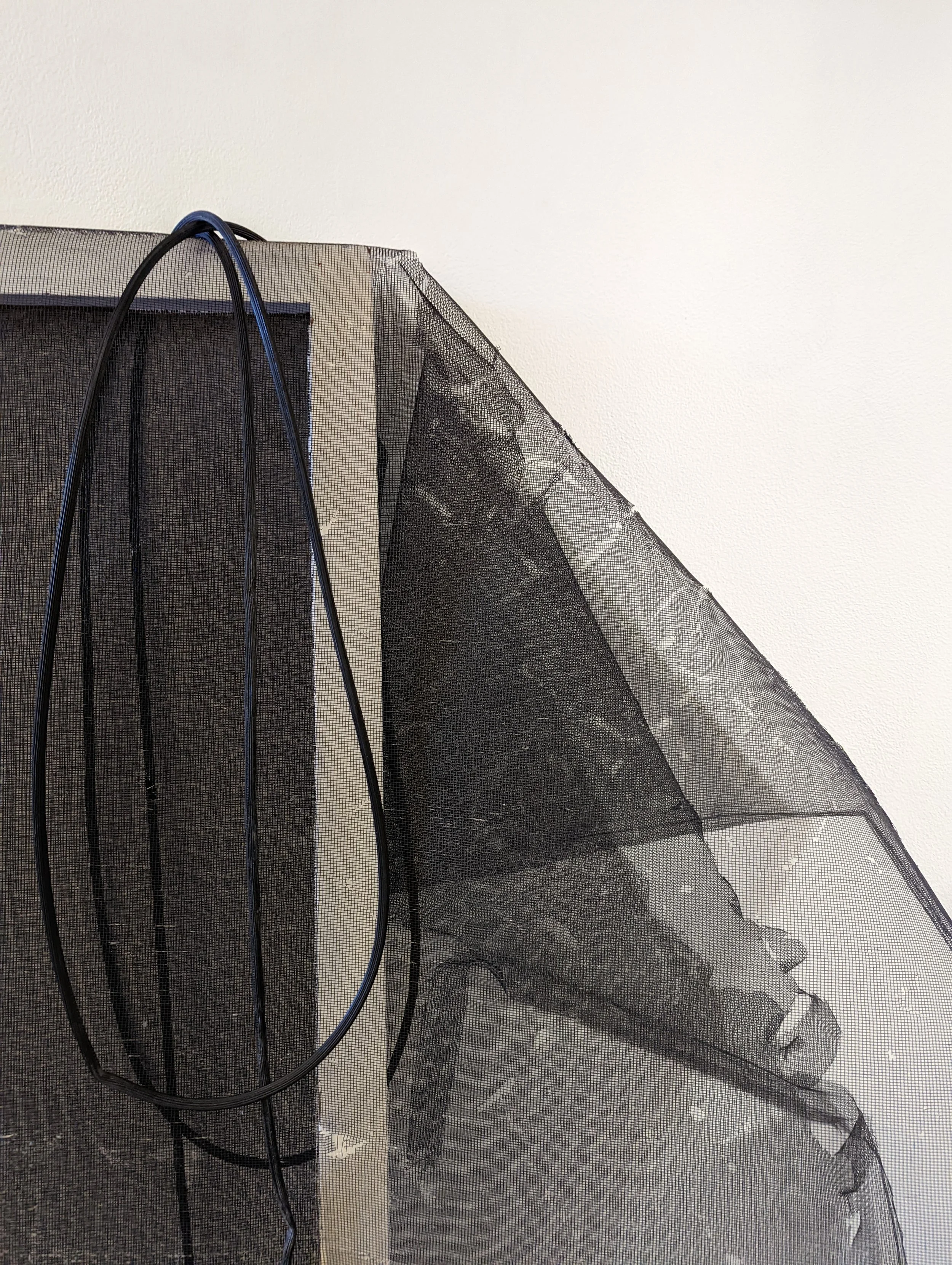 Close-up of a black mesh fabric with black and blue cables draped over it and a cream-colored wall in the background.