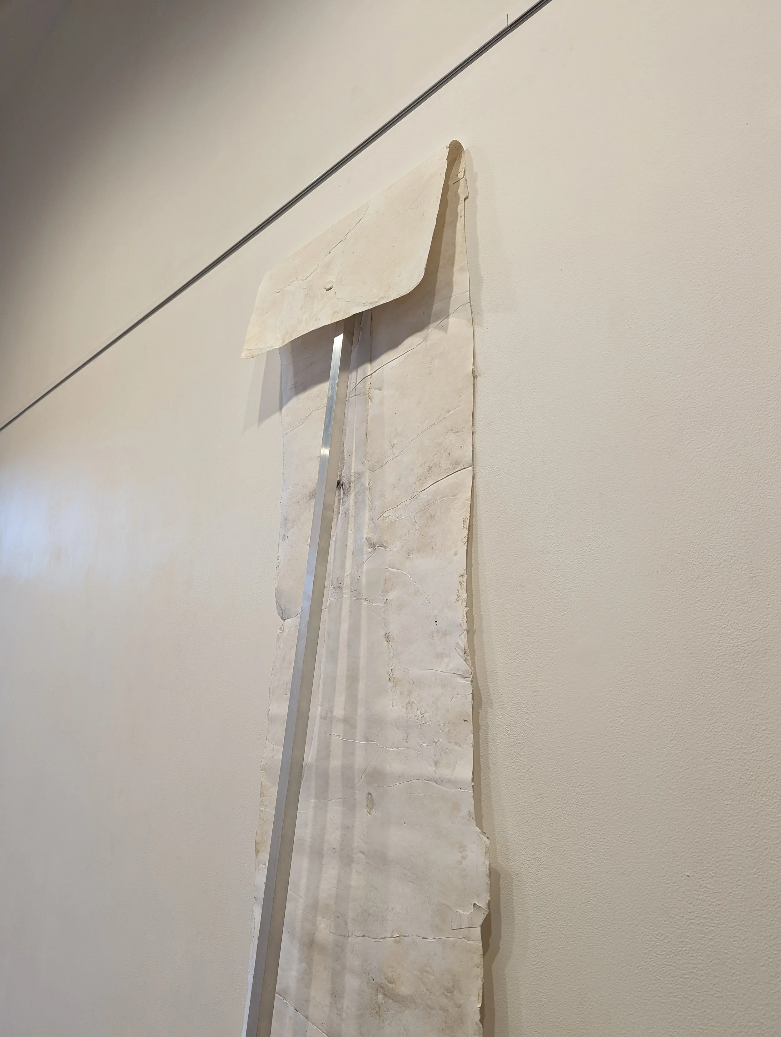 Large, cracked, beige-colored marble slab leaning against a light-colored wall with a metal support rod.