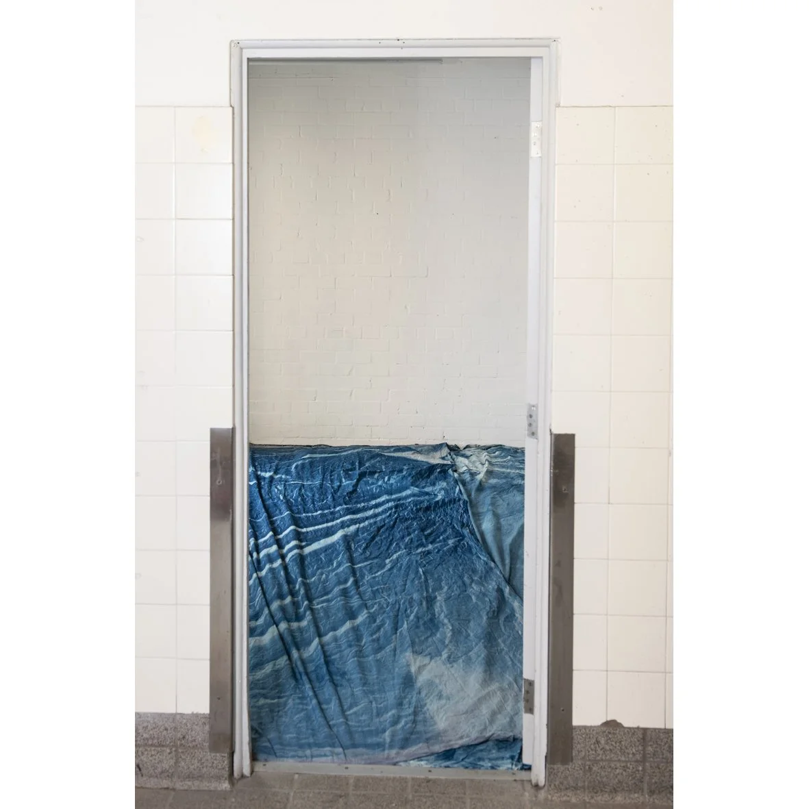 Doorway with a blue tarp covering the entrance, leading to a room with white brick walls.