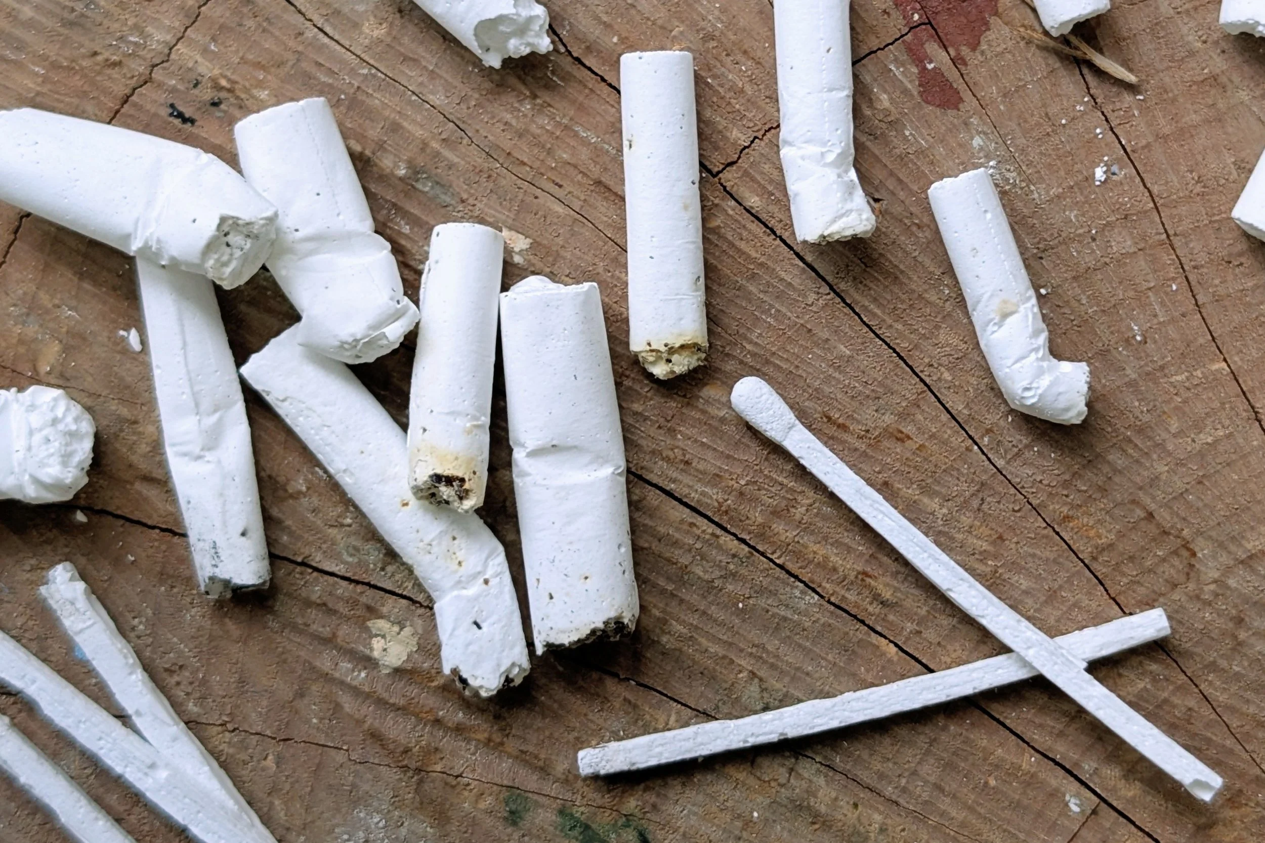 Broken pieces of white chalk scattered on a wooden surface with visible cracks.