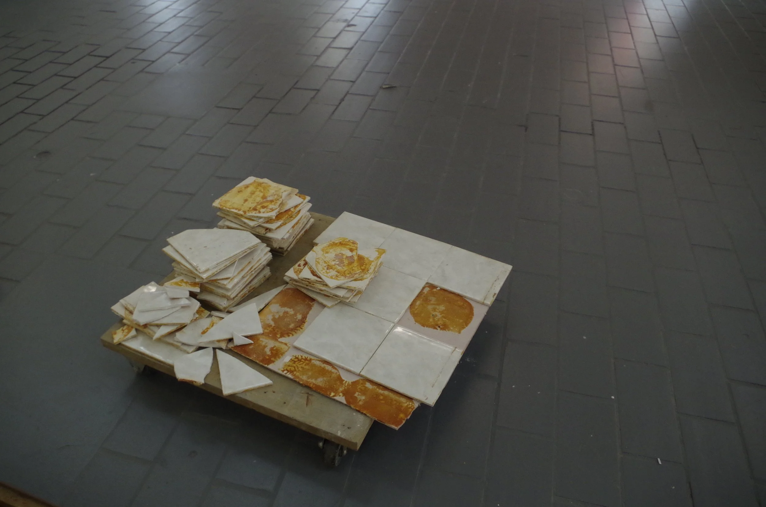 Tile floor with a low table holding a pile of cloths and papers, some stained with a yellowish-brown substance.