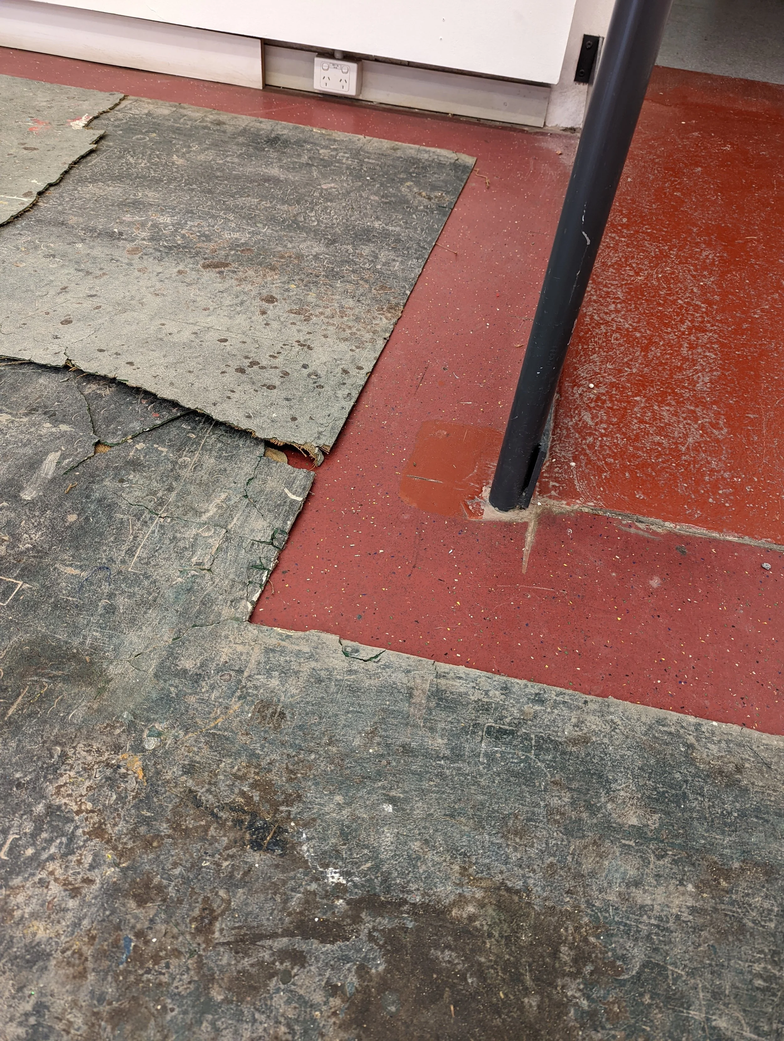 Floor with old, cracked, and worn-out tiles, some of which are missing or damaged, and a black metal pole nearby.