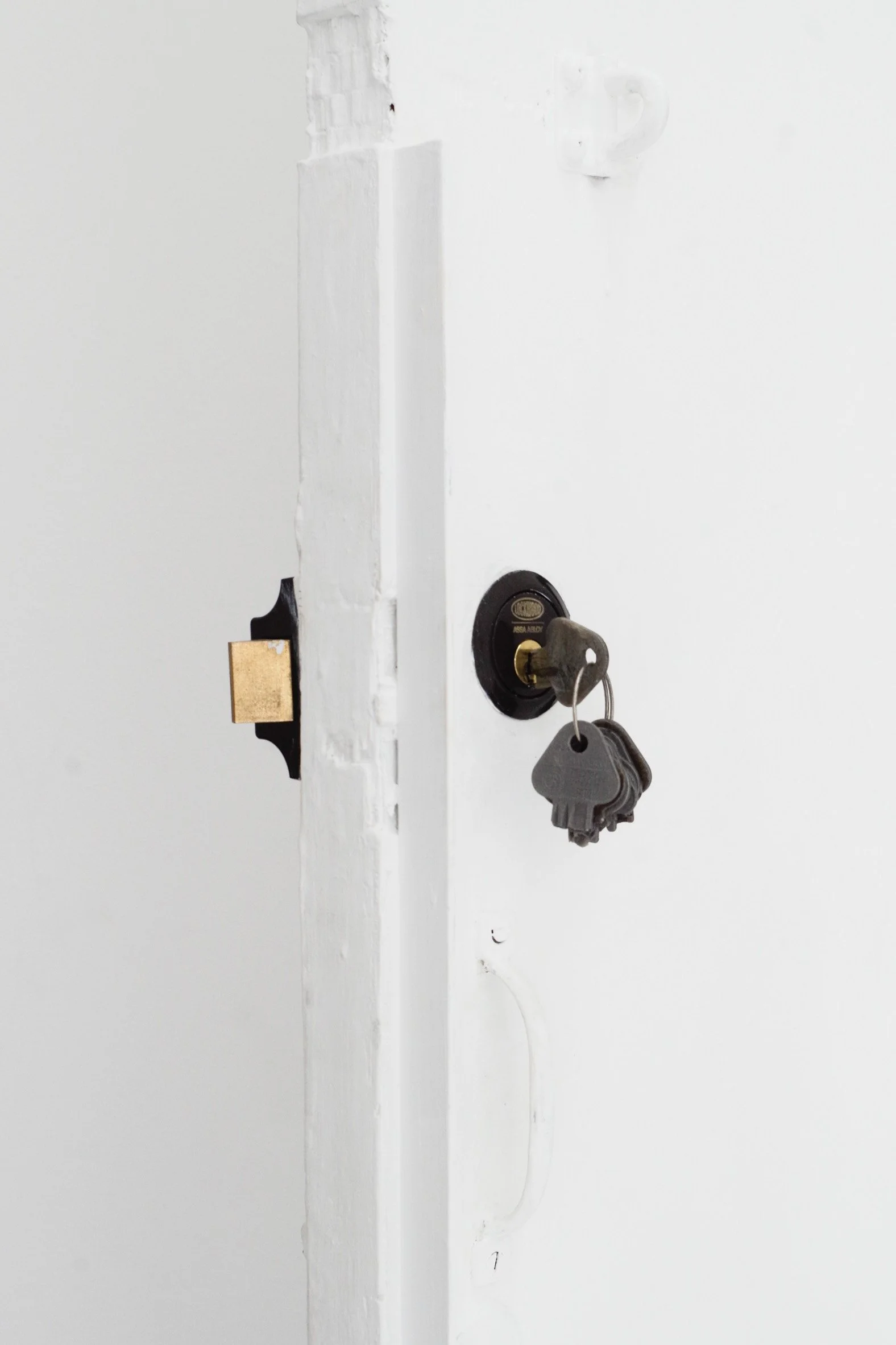 A wall with a door lock and a set of keys hanging from the lock, with a piece of masking tape attached to the door frame.