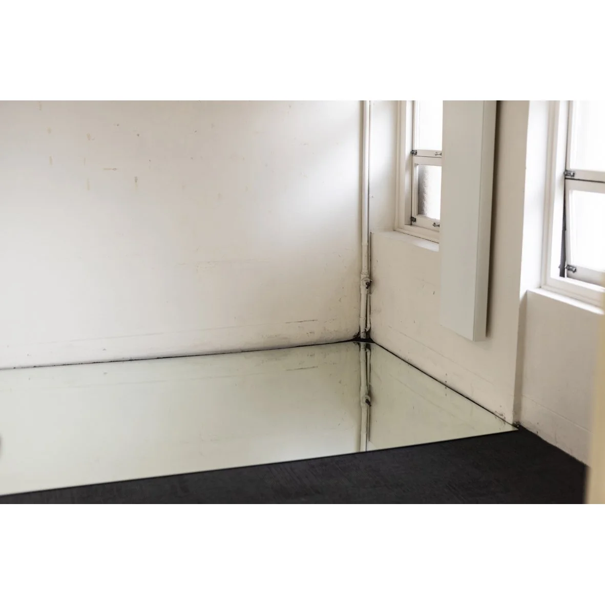 Interior corner of a room with two windows on the right, white painted walls with some marks, and a black carpeted floor.