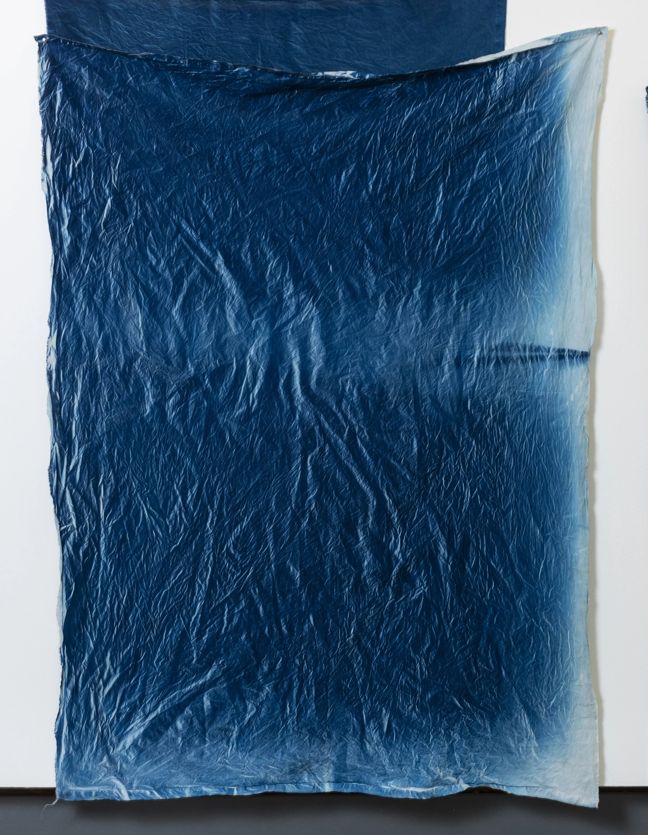 A piece of crinkled blue plastic or fabric hanging on a white wall with a portion of a dark surface below.
