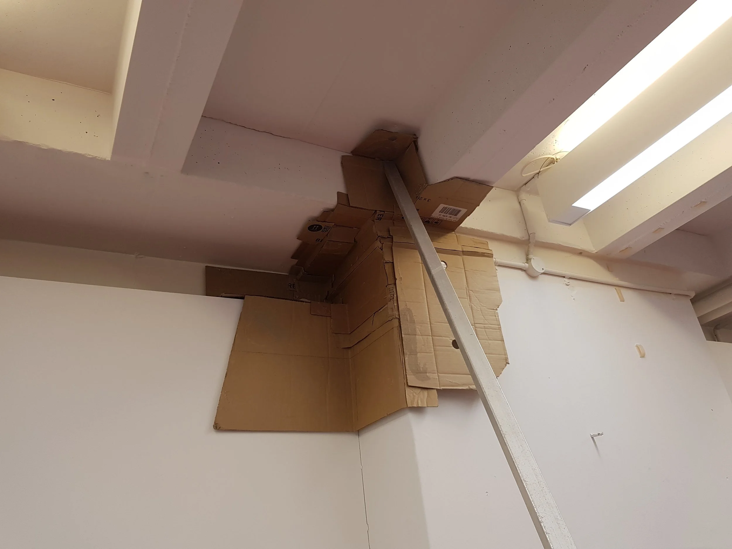 Interior room with white walls, stacked cardboard boxes, and a fluorescent ceiling light.