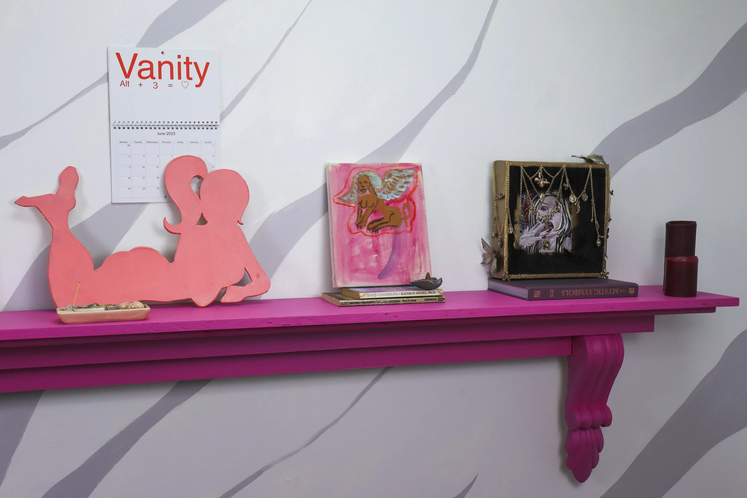 Decorative pink shelf with art and jewelry on a white wall with gray stripes.