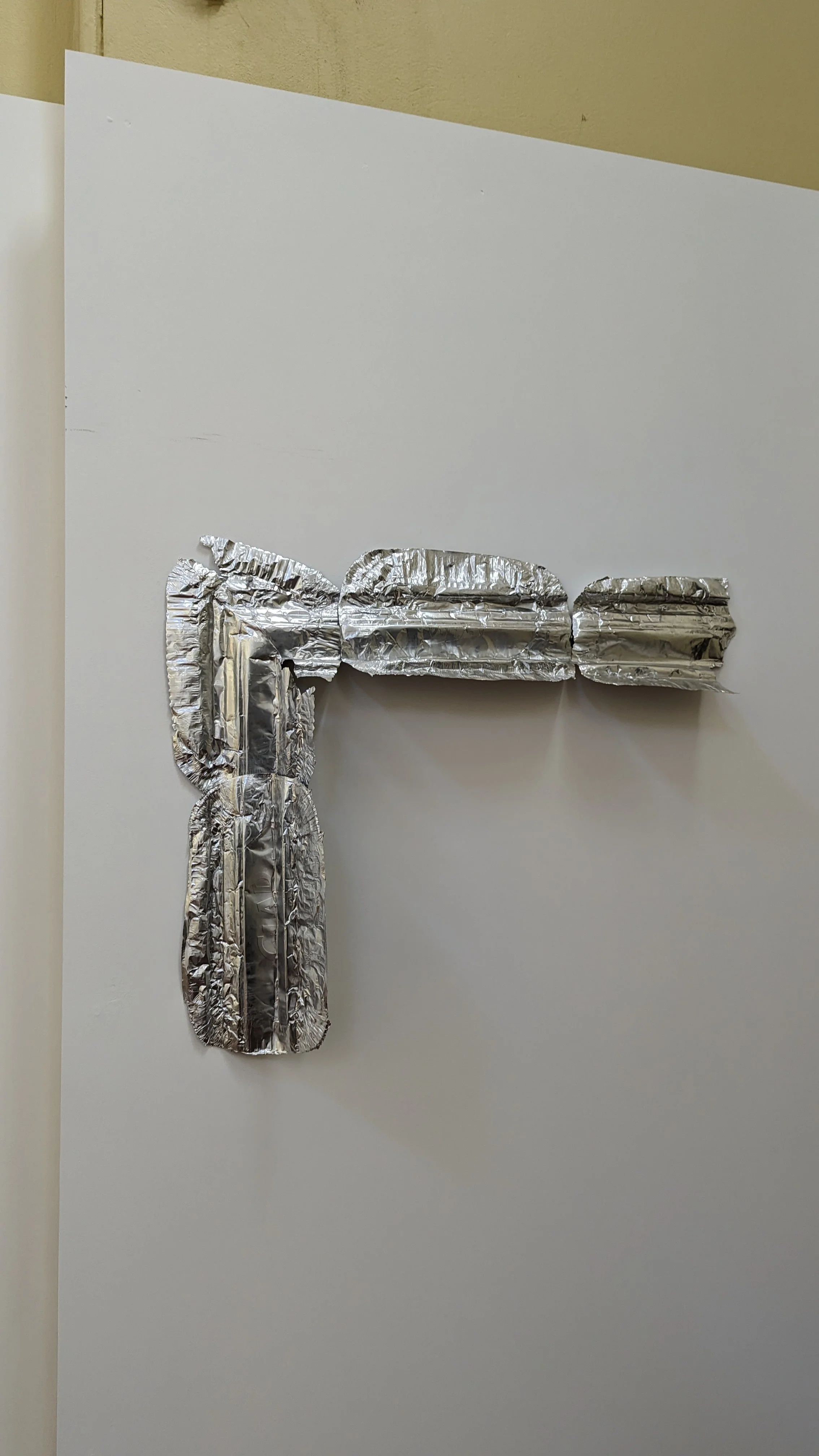 A white sheet of paper with a pipe cleaner shape attached to it, resembling the letter T, made from crumpled and twisted aluminum foil.