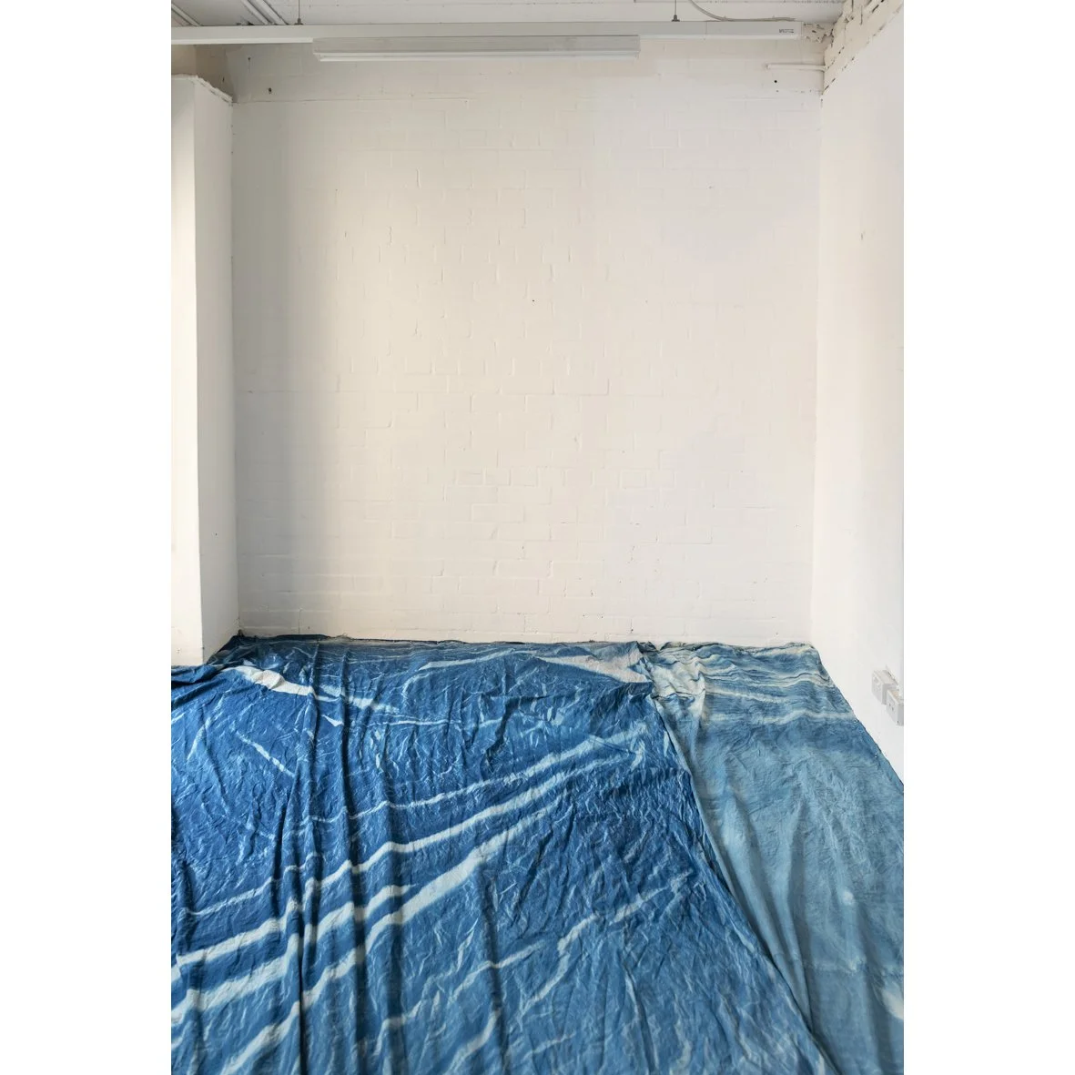 A room with white brick walls and a blue and white tie-dye blanket or sheet spread on the bed or floor.