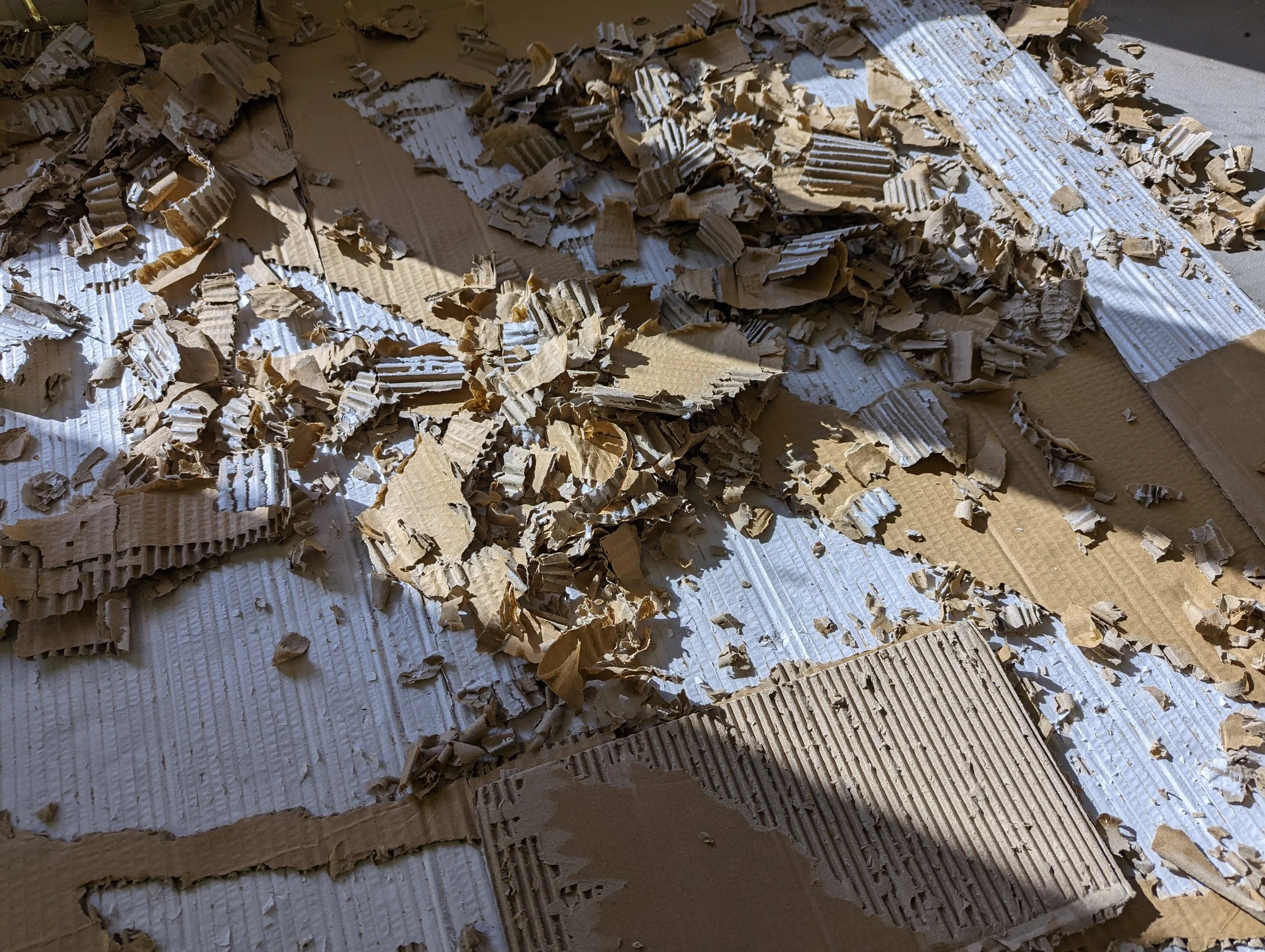 A pile of torn and shredded corrugated cardboard on a surface, with some shadows and sunlight.