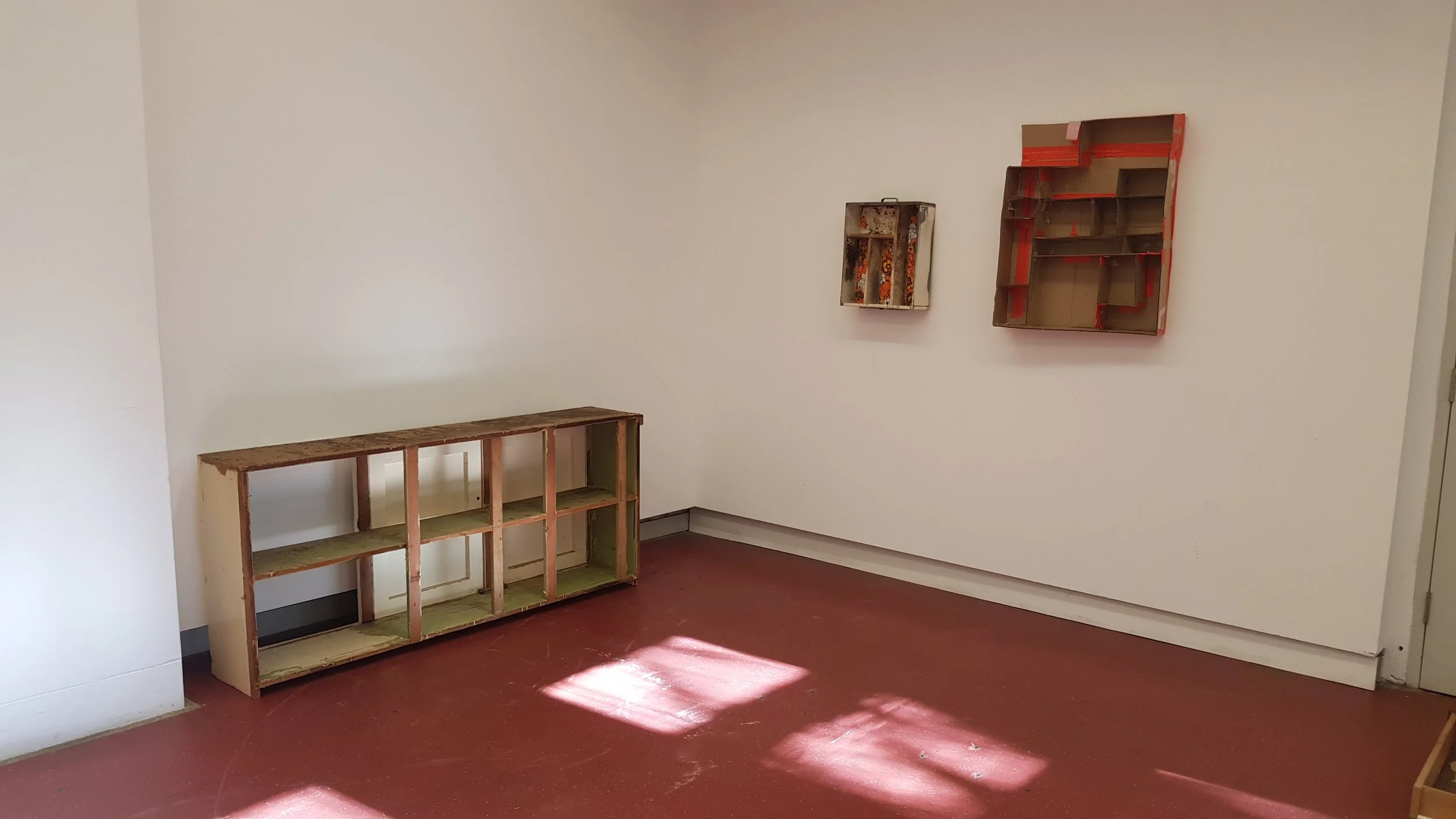 Empty room with unfinished wooden shelves on the wall and a red-brown floor.