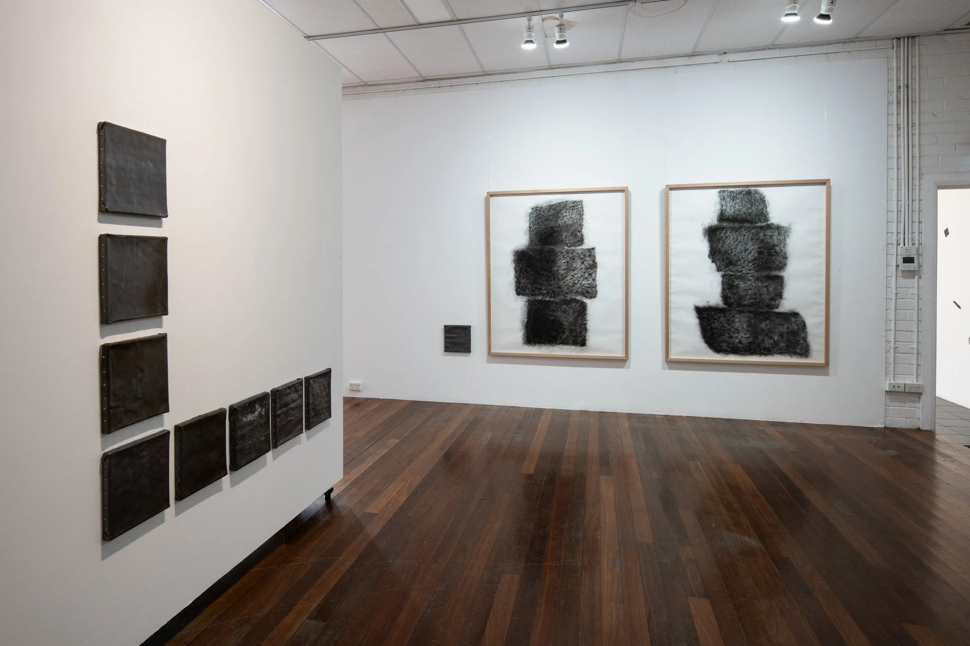 Gallery with abstract artwork, including two large framed black and white pieces on the far wall, and smaller black textured pieces on a white partition wall to the left.