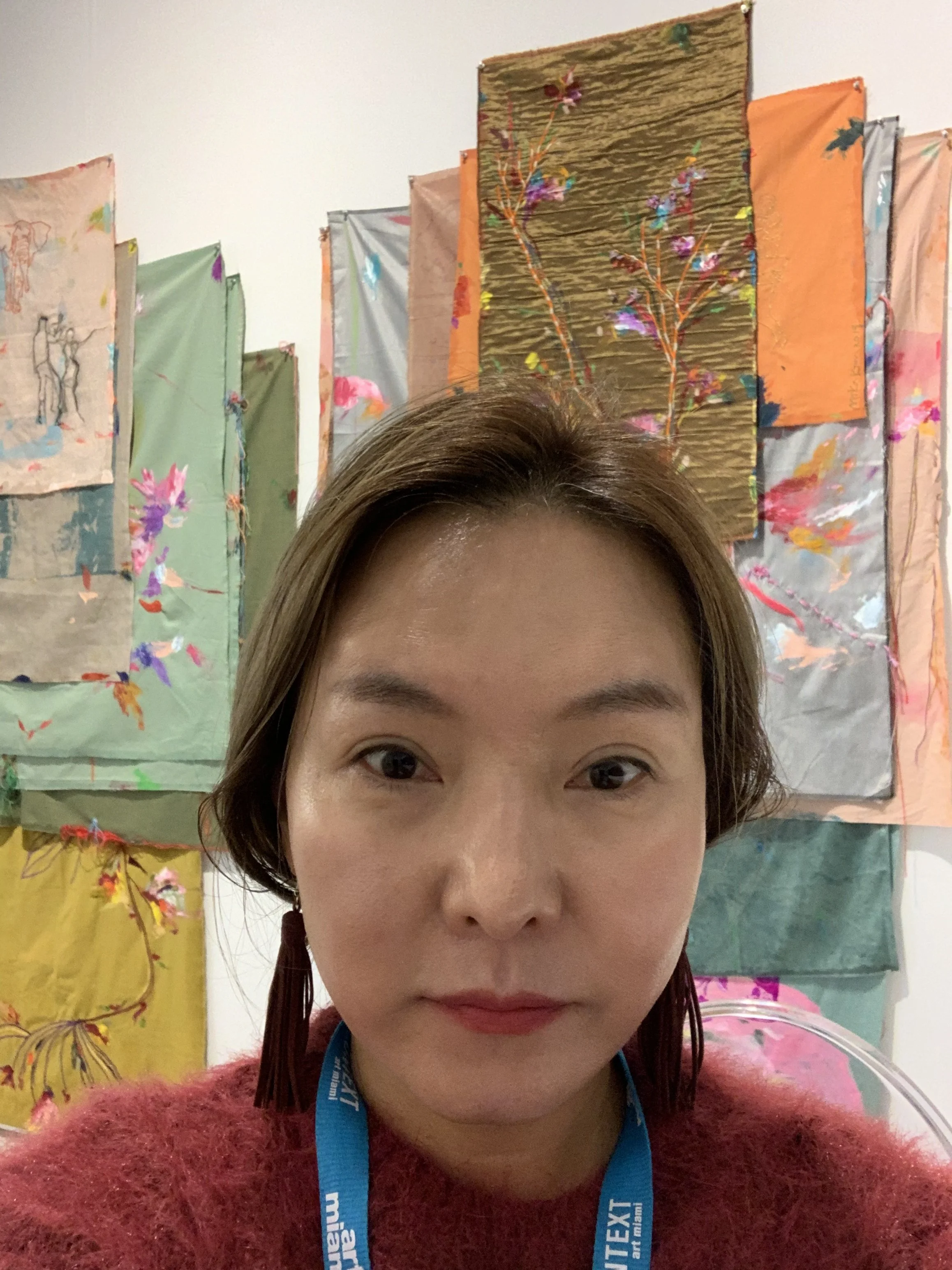 Artist Mika Kim in her studio surrounded by colorful abstract paintings.