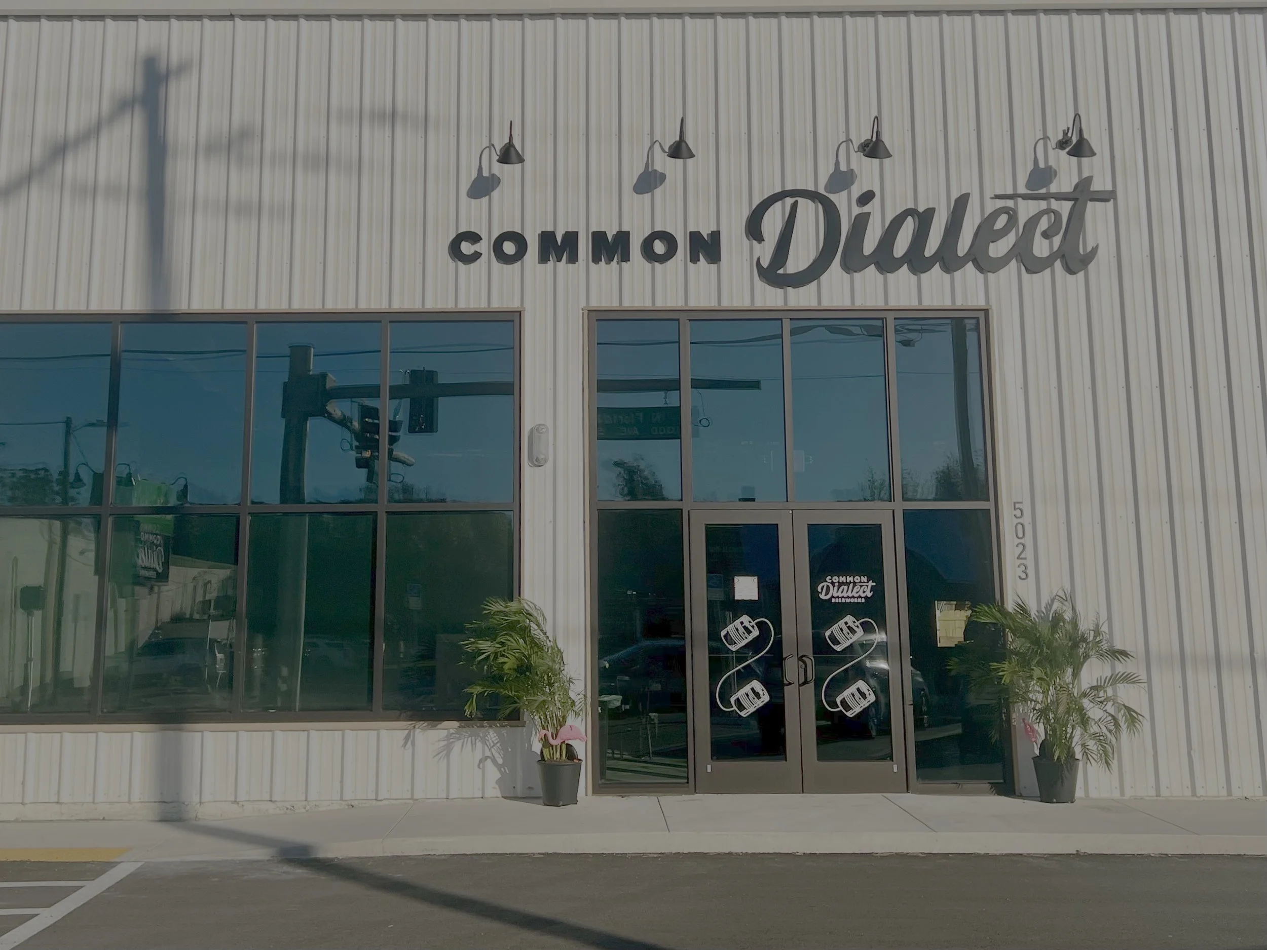 Front view of a modern building with large glass windows and sign reading "Common Dialect" on the exterior, with potted plants near the entrance.