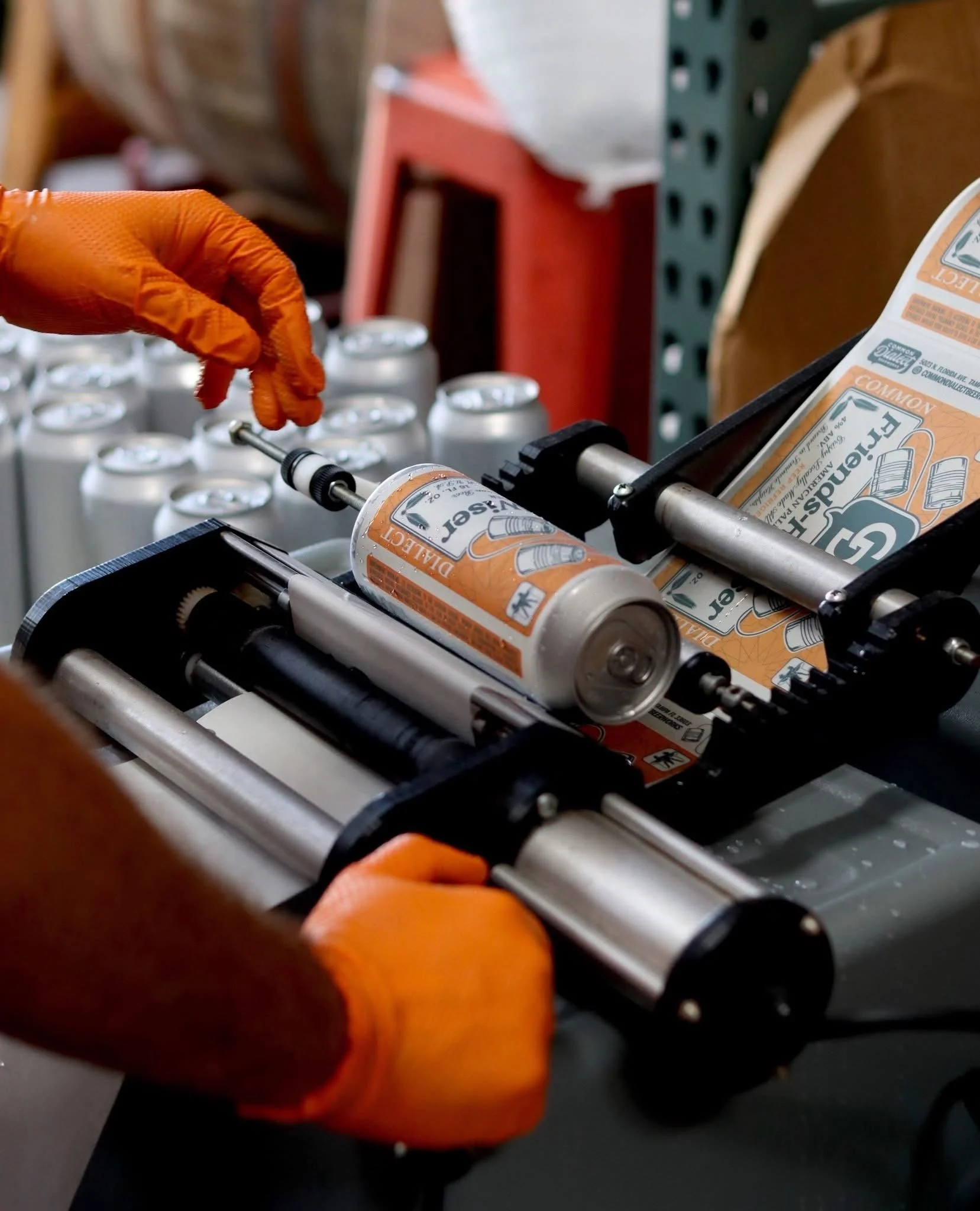 Close-up of a conveyor belt carrying orange boxes labeled 'DANGER' and 'WARNING,' with a person wearing orange gloves handling the boxes.