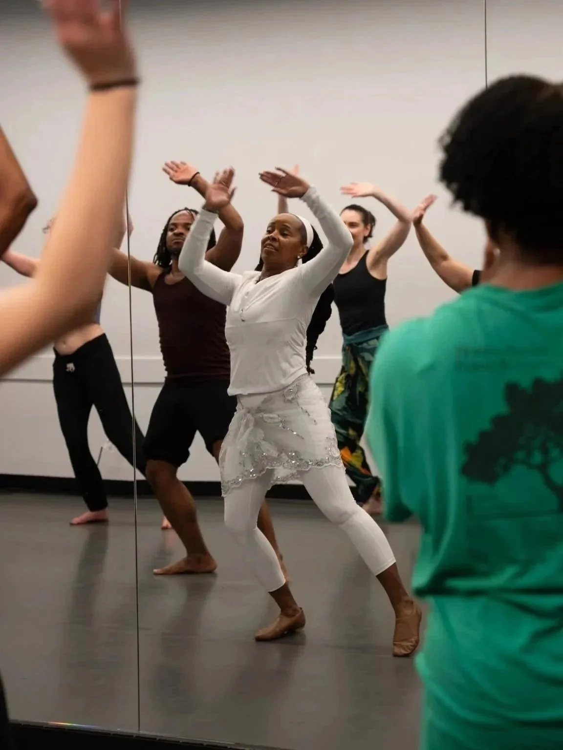 A diverse group of people participating in a dance or fitness class in front of a mirror, with one woman leading the activity.