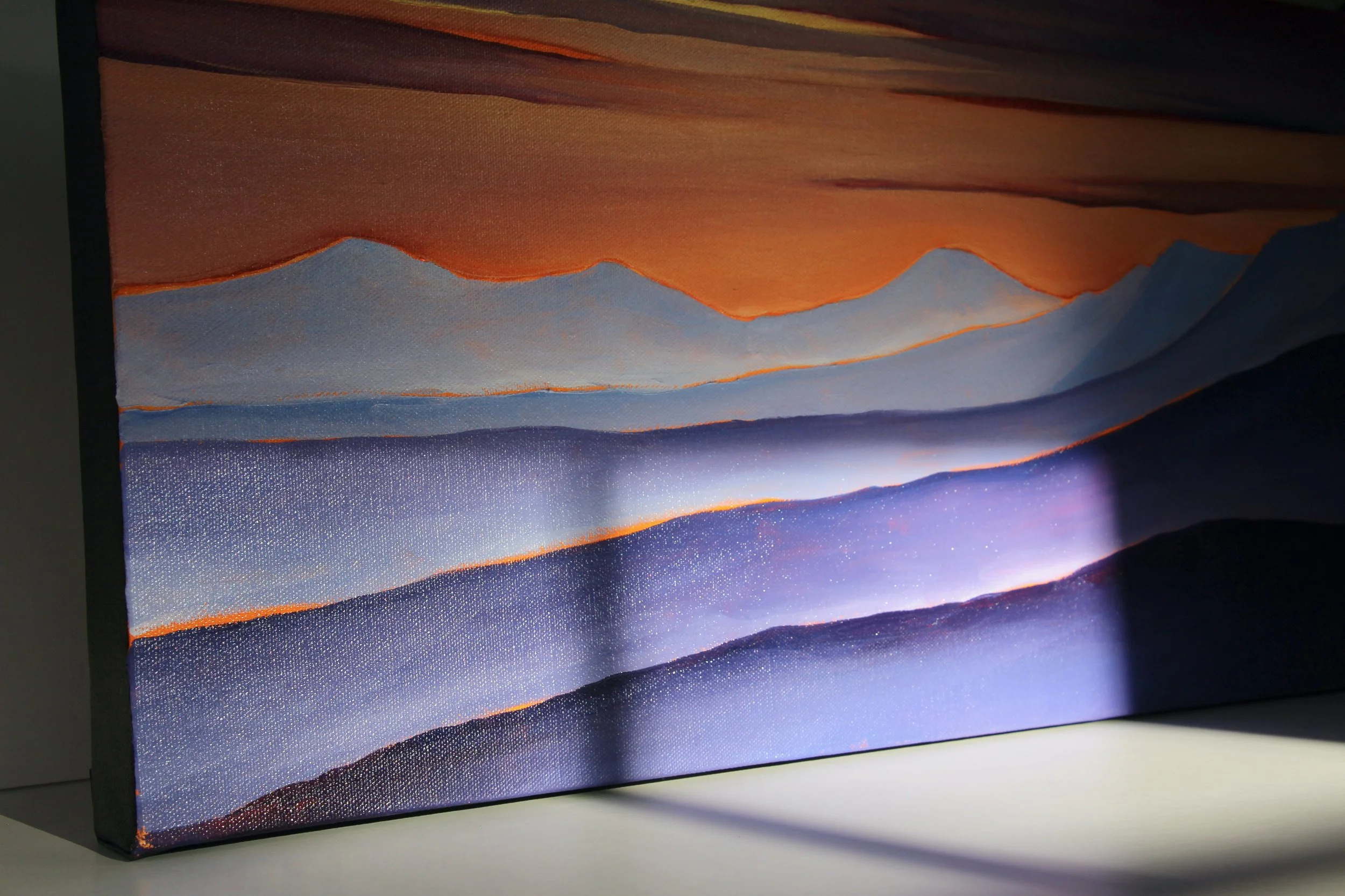 Close-up of a textured painting of mountain ranges at sunset or sunrise with a blend of warm and cool colors.