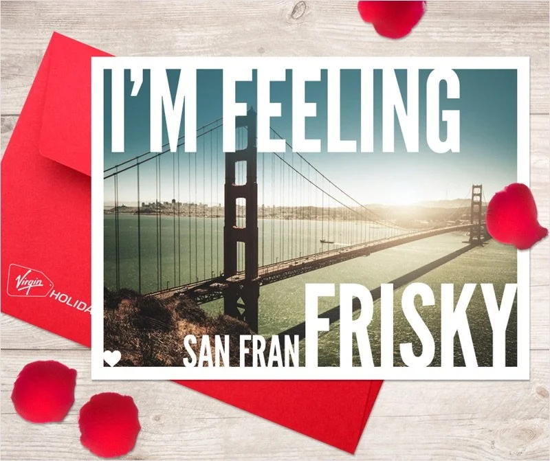Greeting card featuring the Golden Gate Bridge in San Francisco at sunset, with the text 'I'm Feeling Frisky' and 'San Fran' and red rose petals on a light wooden surface with red envelope.