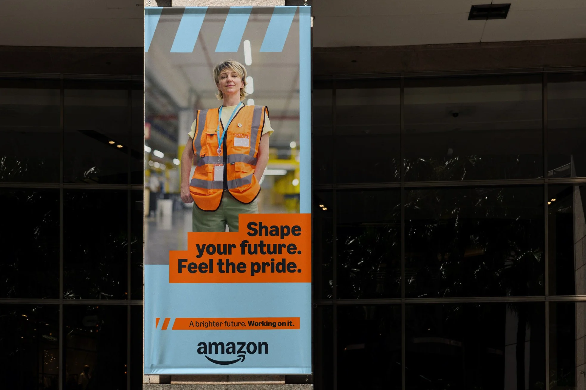 A poster with a woman in a reflective orange safety vest on it. The woman has short blonde hair and is standing with her hands in her pockets. The poster contains the messages "Shape your future. Feel the pride." and "A brighter future. Working on it