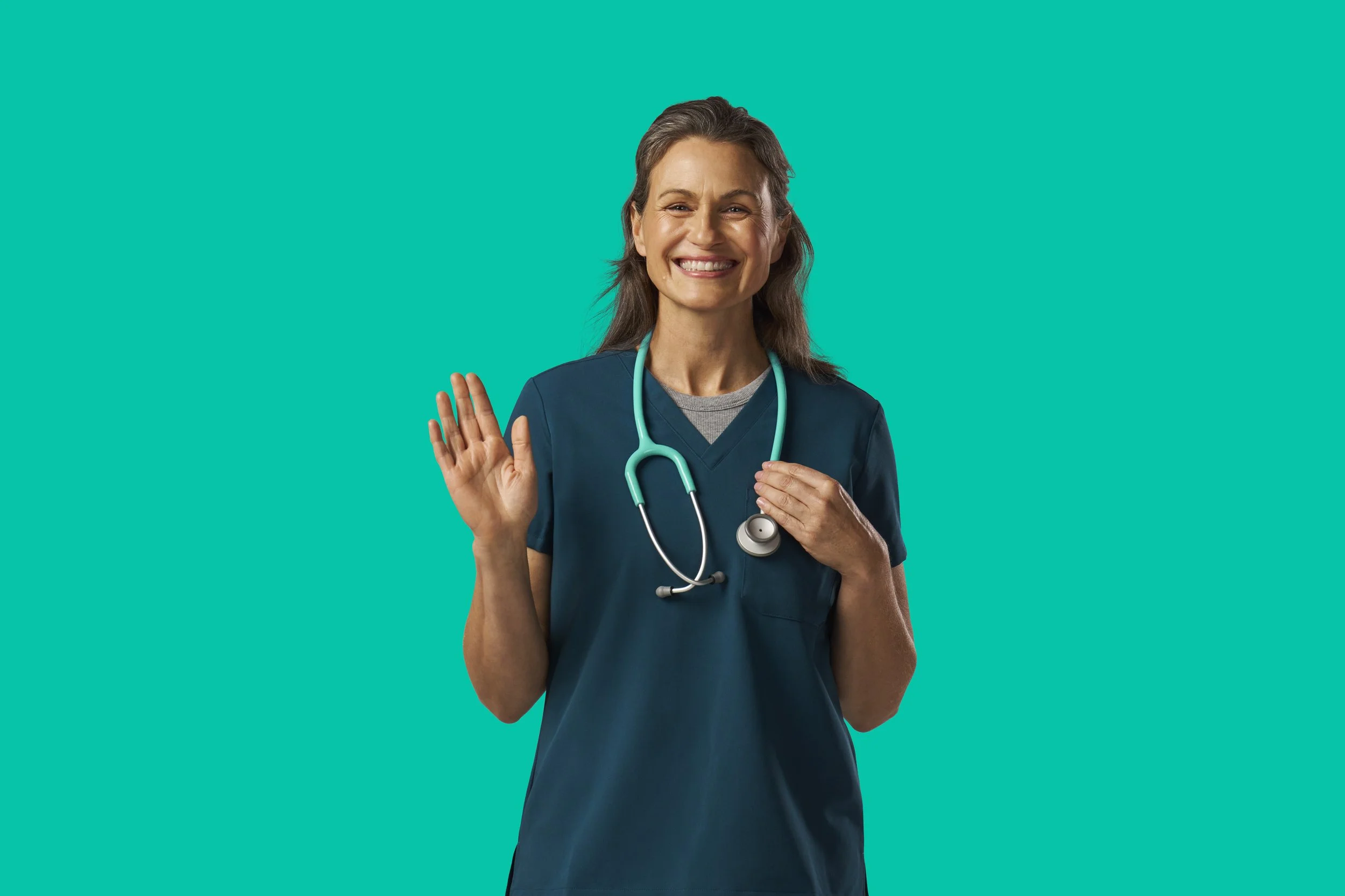 A smiling female healthcare professional in scrubs with a stethoscope around her neck, waving.