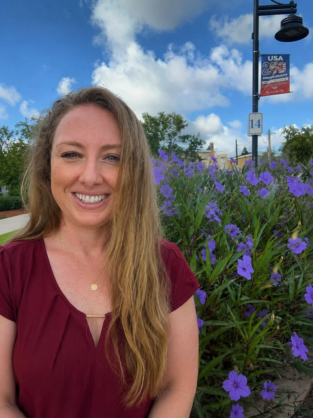 Alison Stohler, founder of Peace of Mind Care Visits, smiling outdoors beside purple flowers.