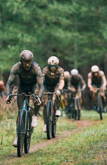 Group of mountain bikers riding on a dirt trail through a green, wooded area.