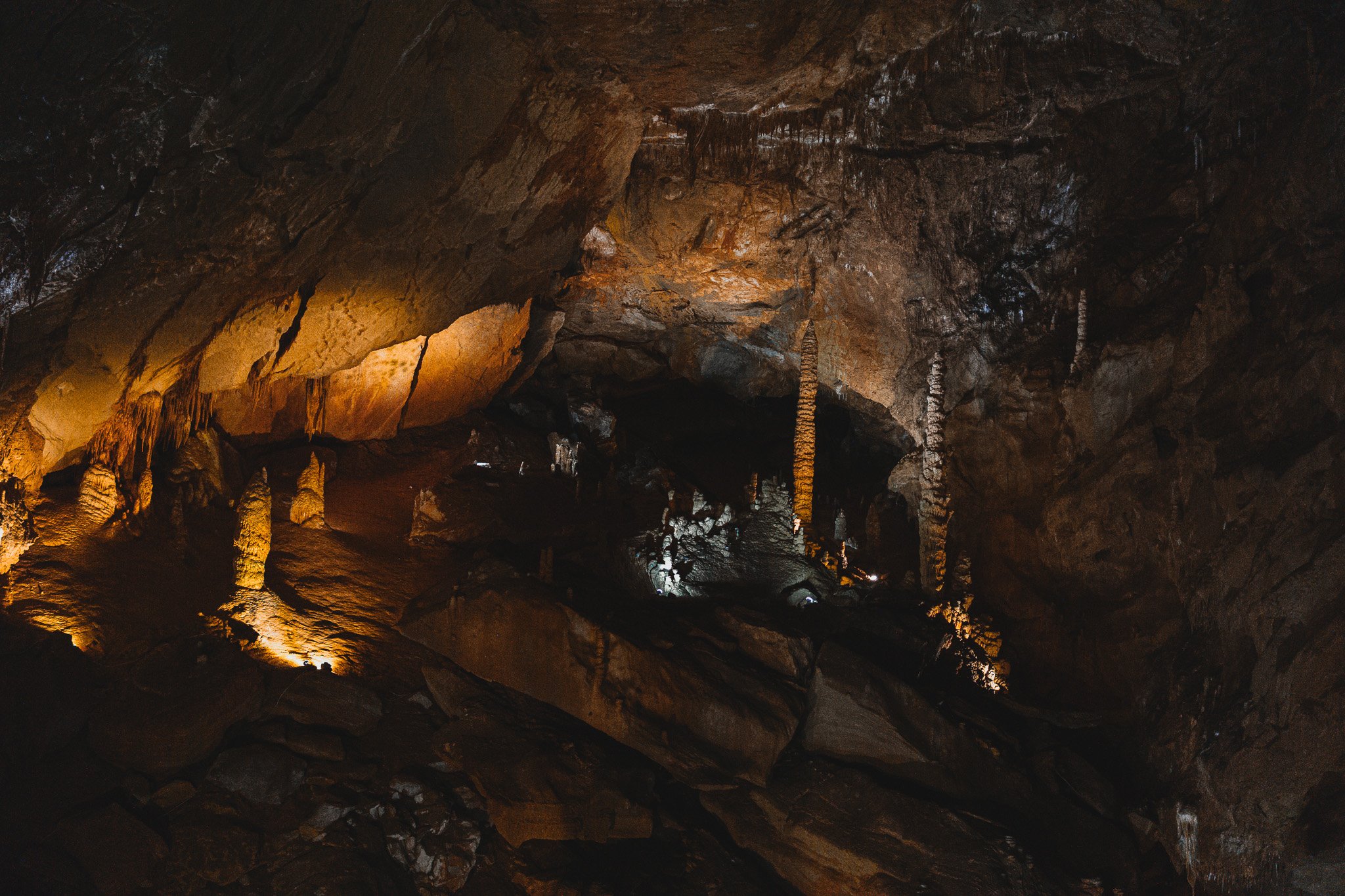A view of a cave with stalactites and stalagmites illuminated by warm lights.