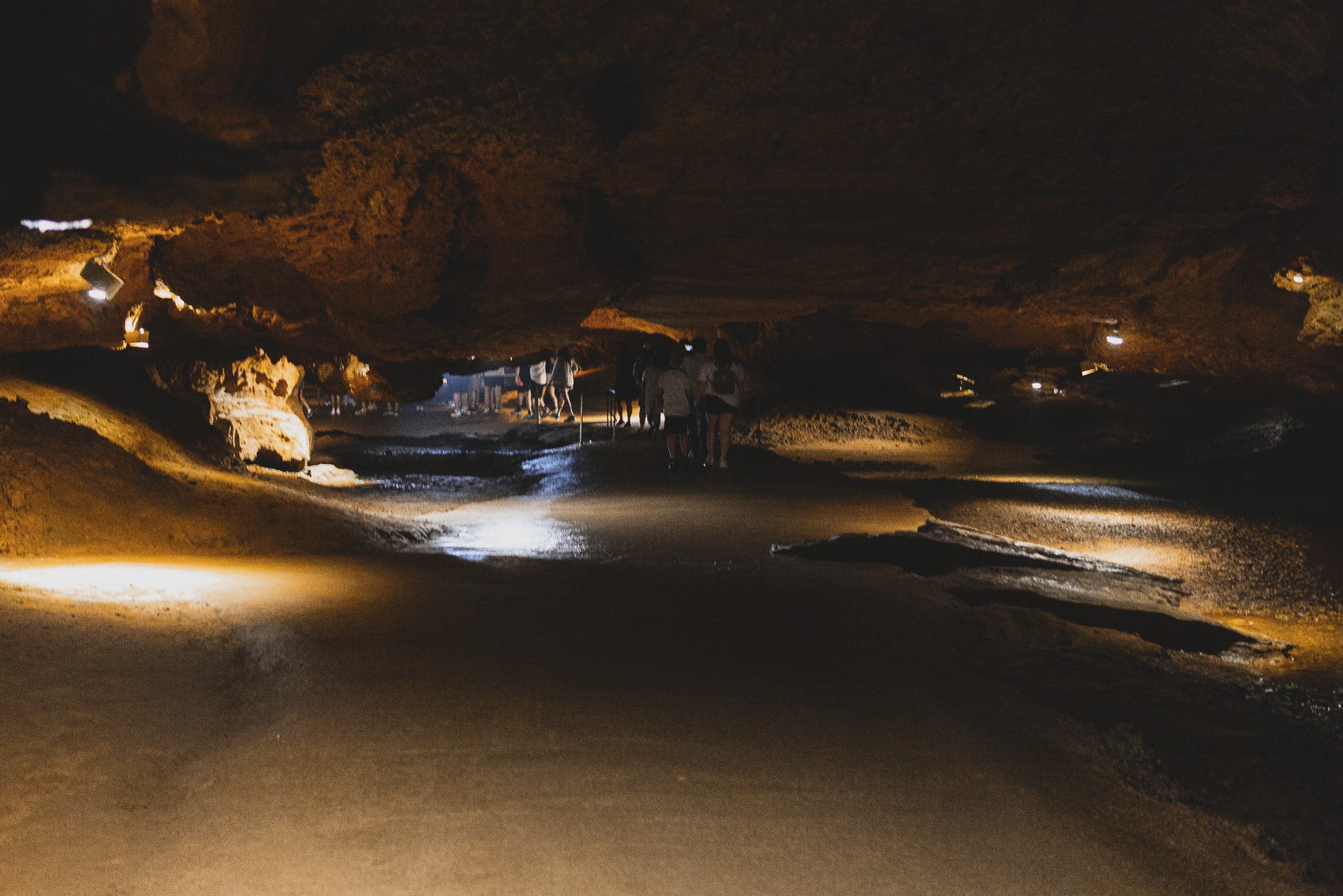 People exploring a dark cave with illuminated pathways and rocky formations.