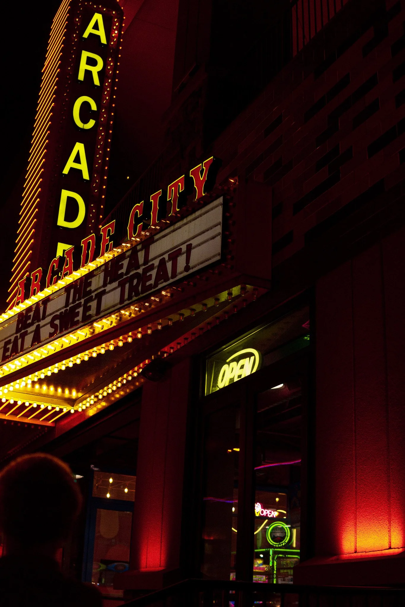 Nighttime view of a theater marquee with illuminated yellow and red letters advertising a show. The marquee displays the words 'ARCAD' vertically and 'THE GREAT GATSBY' along with other text that is not fully visible. There are bright lights outlinin