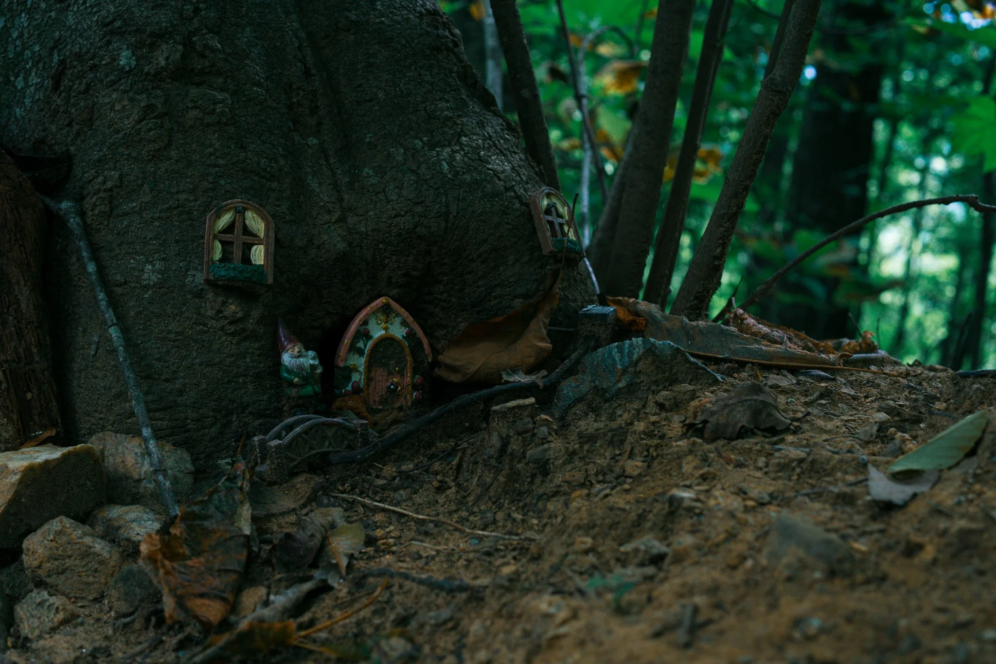 Small decorative house ornaments with tiny windows and doors, placed against a dark tree trunk in a forest setting.
