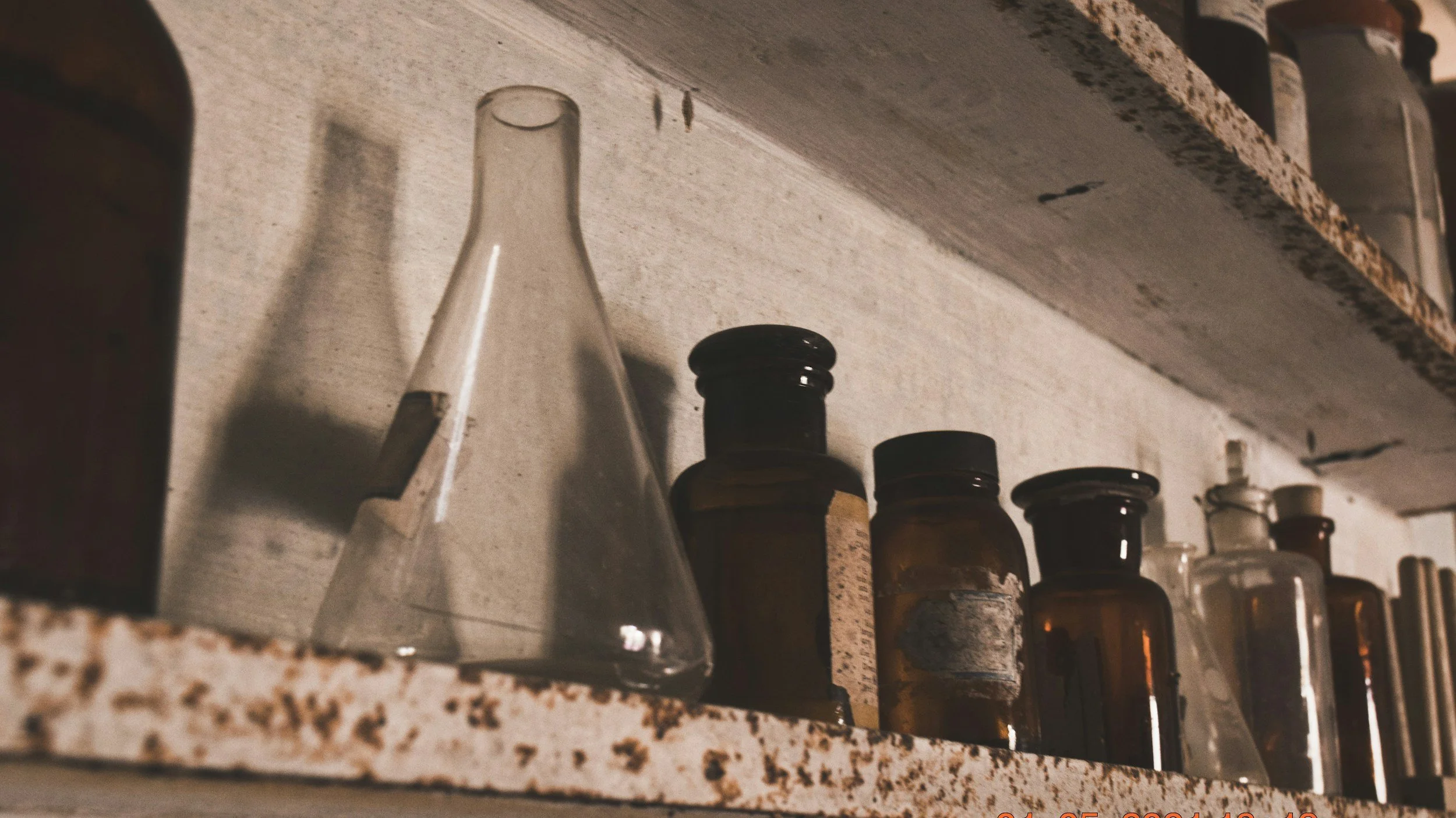 A collection of medicine bottles and a glass container on a kitchen shelf, with a rough granite countertop above and a backsplash behind.