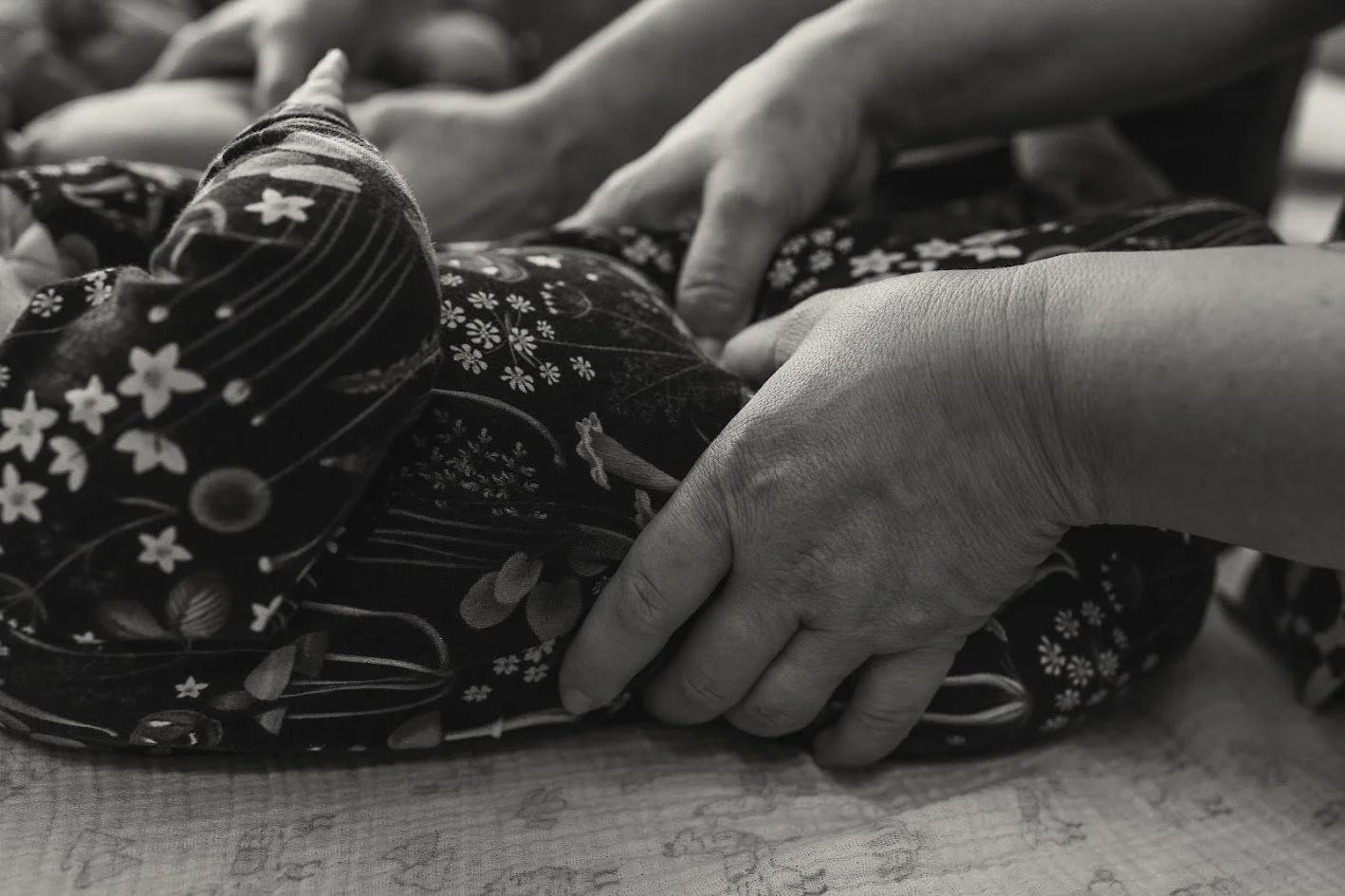 Close-up of a person's hand resting on a fabric with floral patterns, black and white photo.