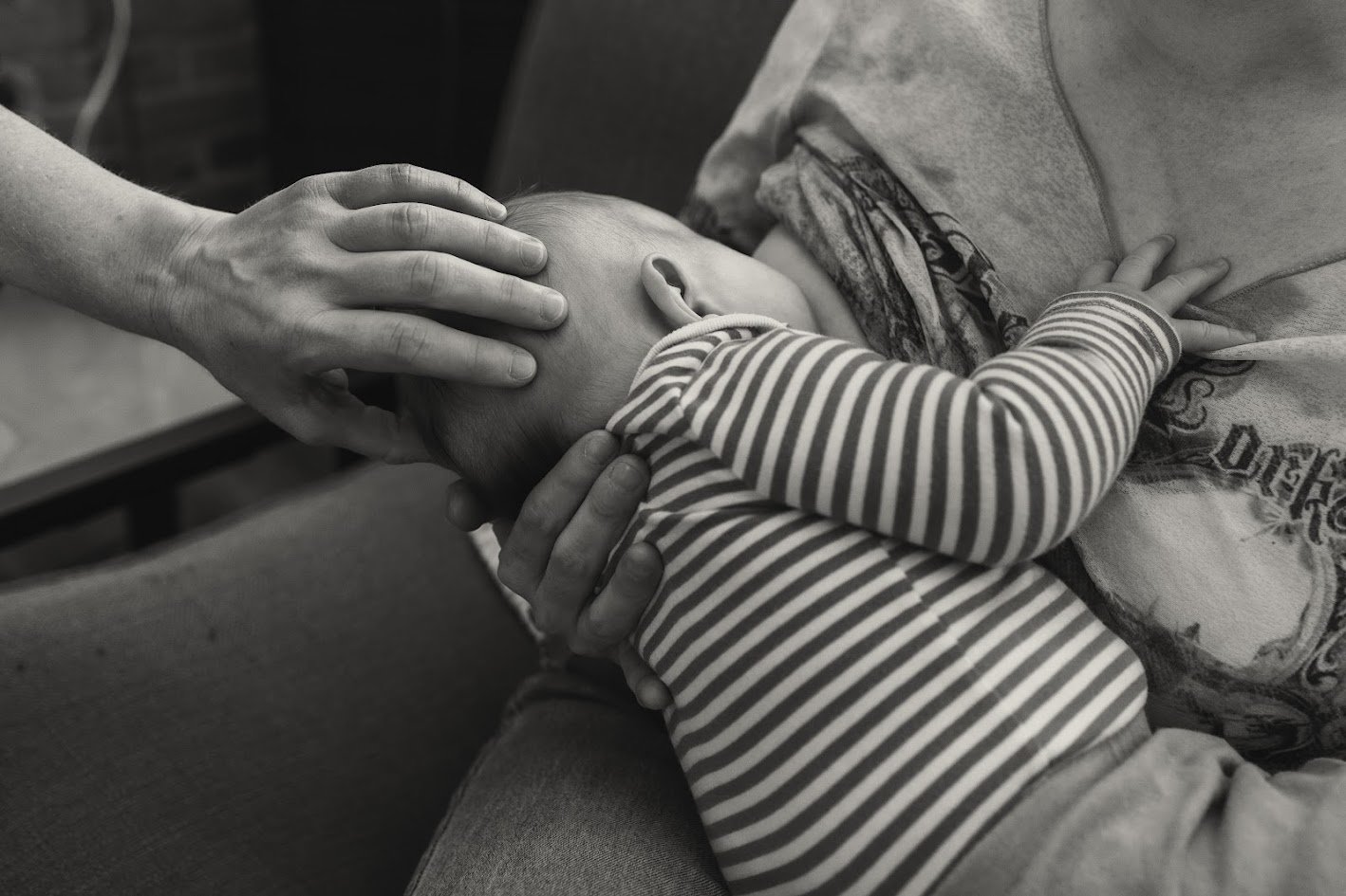 A child leaning on an adult's lap with their head pressed against the adult's chest, while an adult's hand gently rests on the child's head in a comforting gesture.