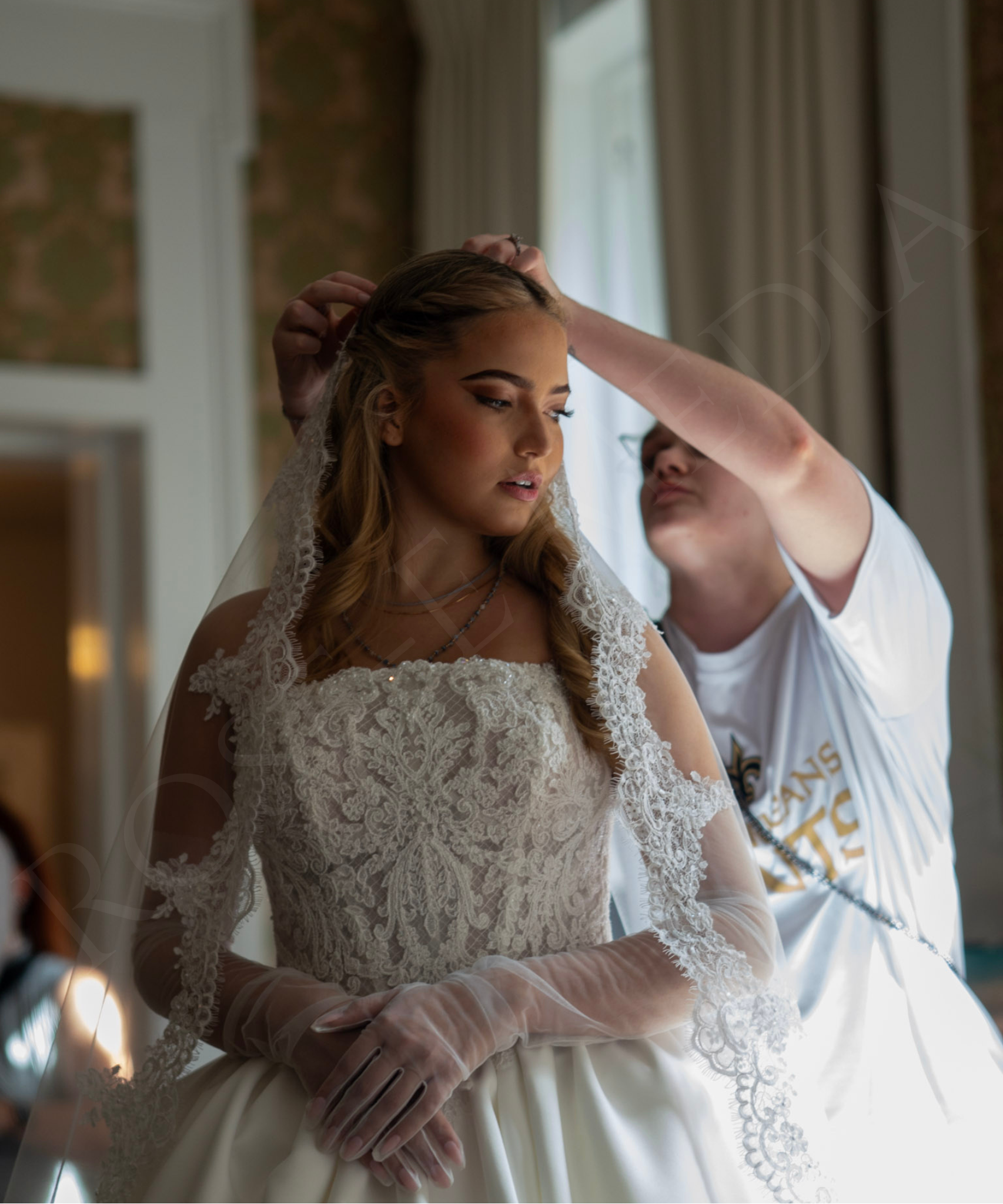 A behind-the-scenes moment from a NOW Weddings editorial shoot at the Malaga Inn in Mobile, capturing the final styling touches as a veil is placed on the model before the next shot.
