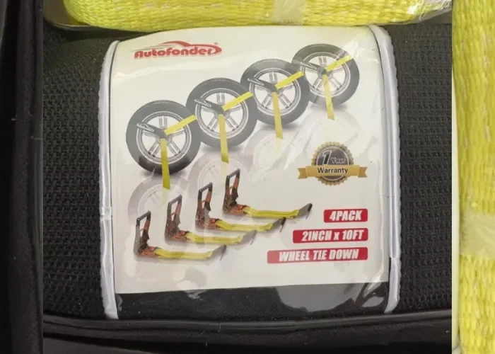 Package of four 2-inch by 10-foot wheel tie-down straps with rubber-coated hooks on a black surface.