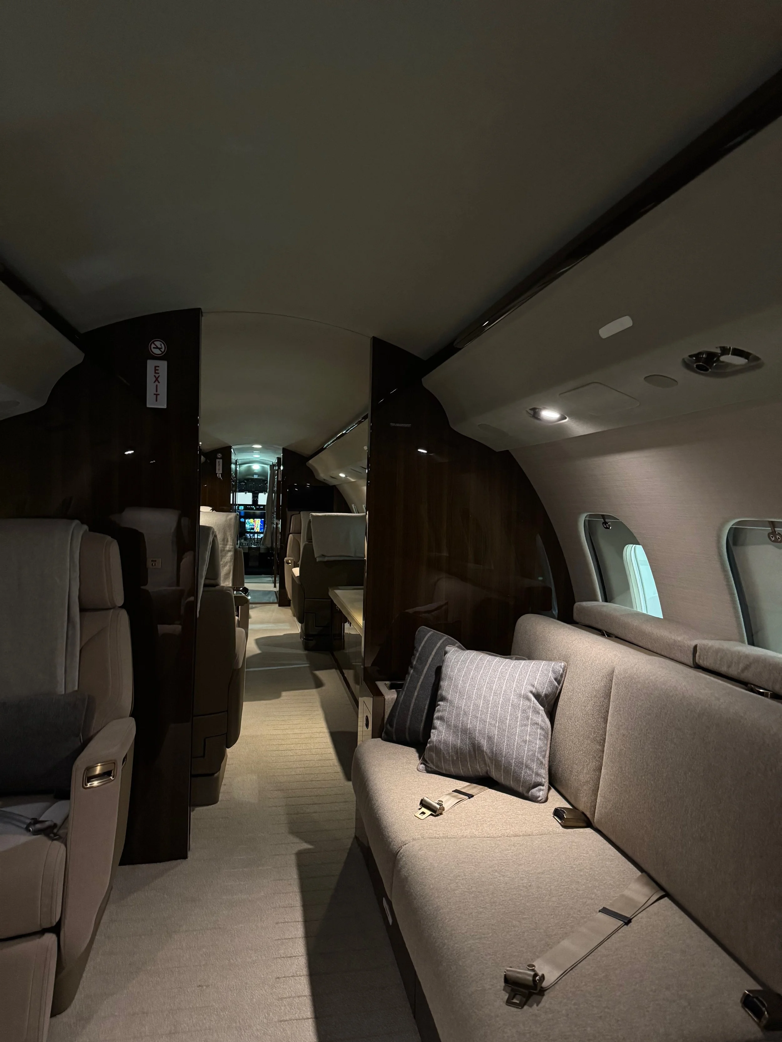 Interior of a private jet with beige seating, a gray pillow on one seat, and wood paneling.