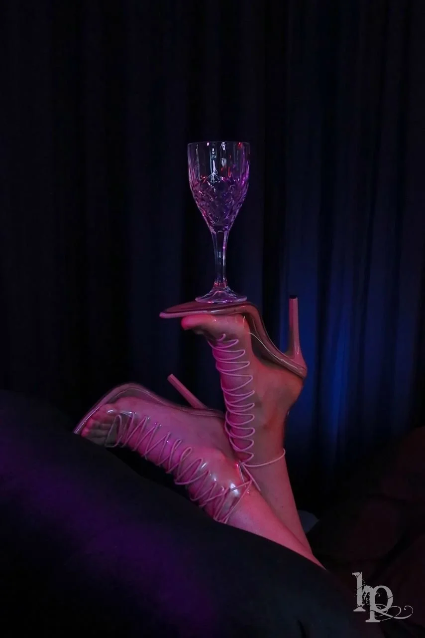 Wine goblet balanced on balls of feet in laced clear stilletto heels 