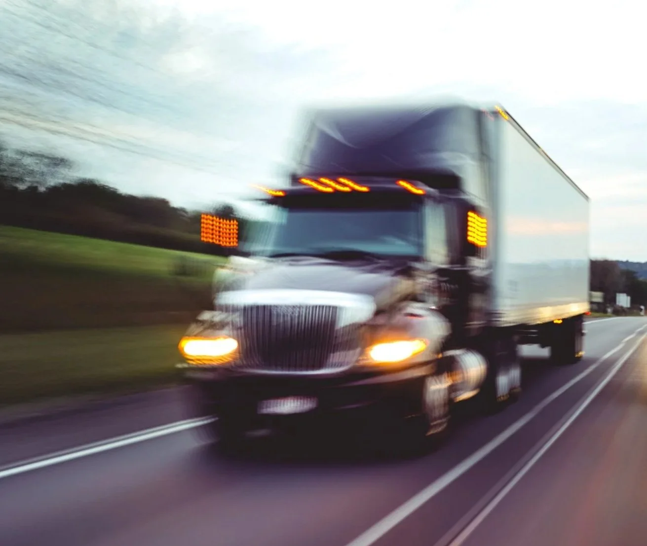Moving black semi-truck driving on a highway during dusk.