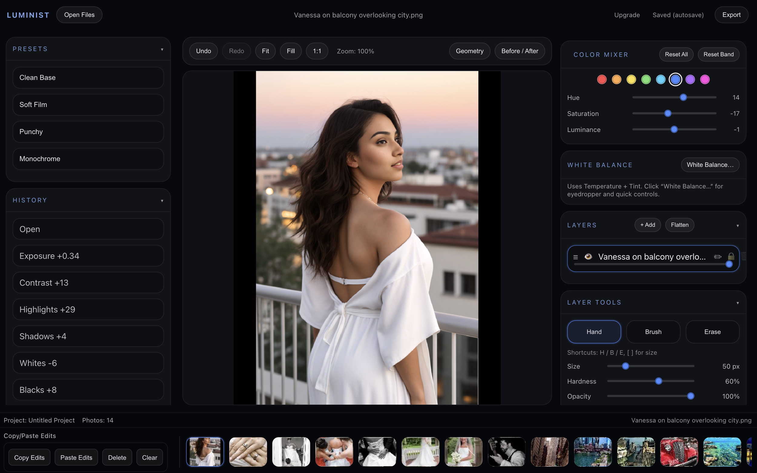A woman with long, wavy dark hair and light makeup, gazing to the right, stands on a balcony overlooking a cityscape during sunset, wearing an off-shoulder white dress.