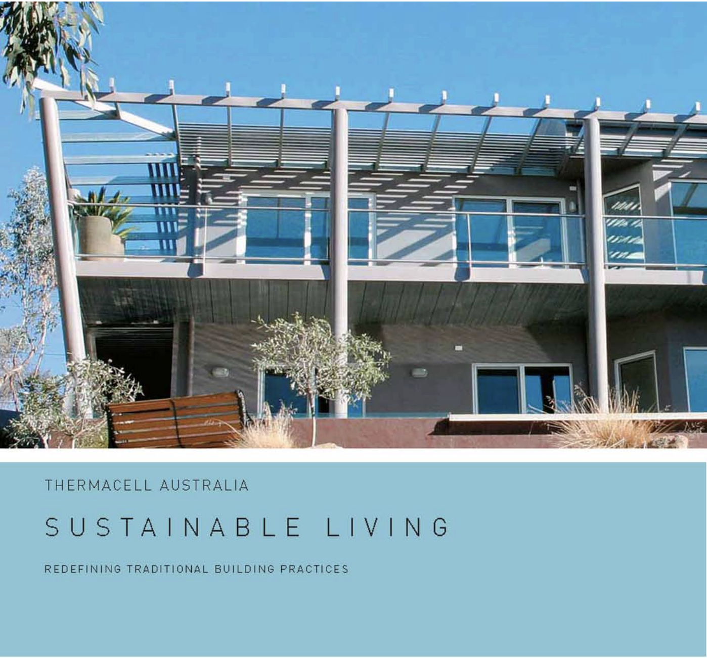 A modern multi-story building with glass balconies and metal beams, surrounded by plants and trees, against a clear blue sky.