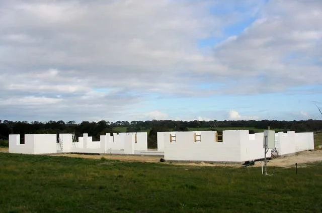 Under construction white building in a rural area with green grass and cloudy sky.
