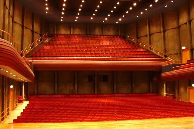 Empty theater with red seats, wooden interior, and ceiling with many small lights.