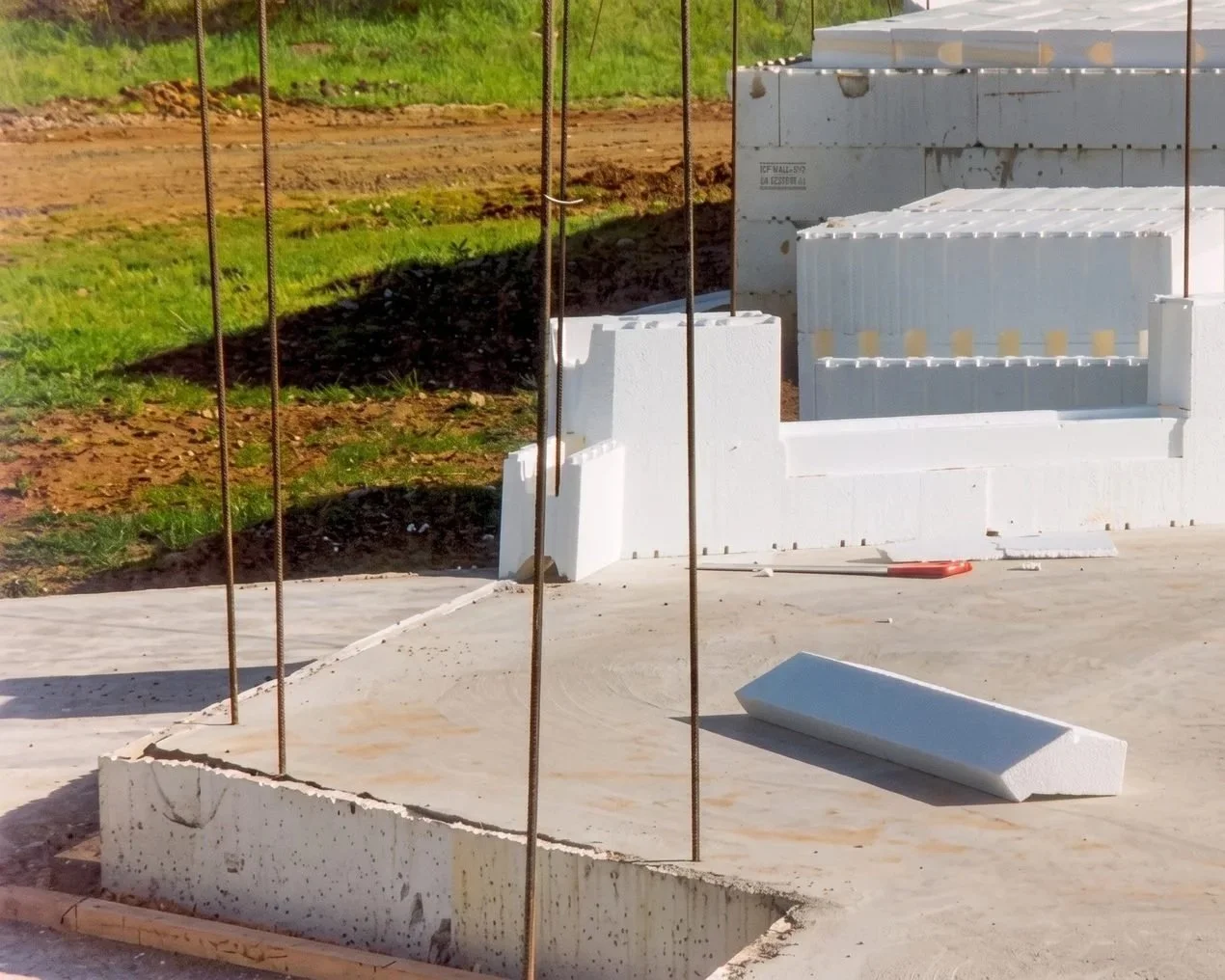 Construction site with concrete blocks, rebar, and foam insulation panels during building foundation work.