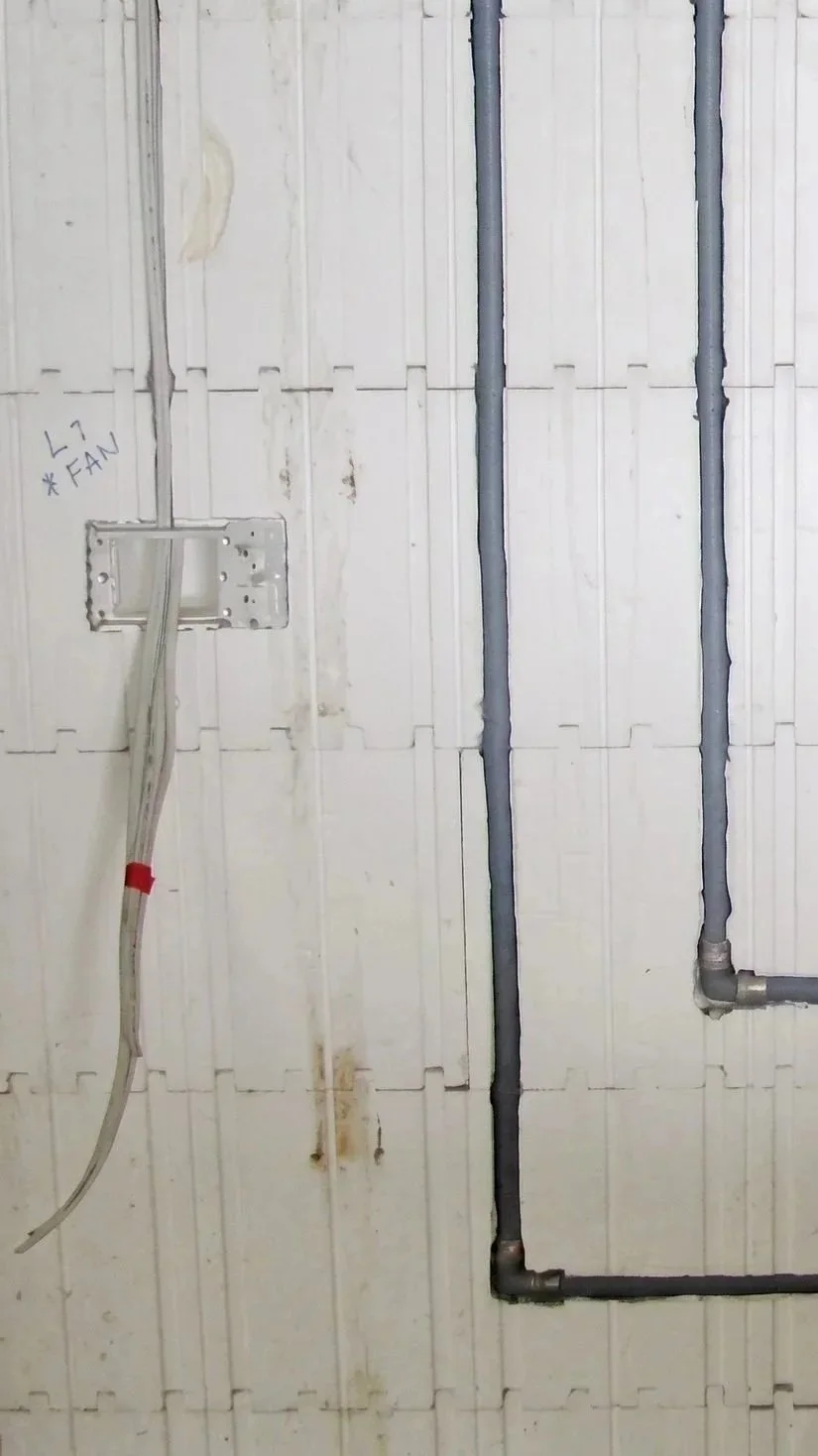 Electrical wiring and conduit pipes on a partially finished wall with a handwritten note labeled 'L7 FAN' near a junction box.